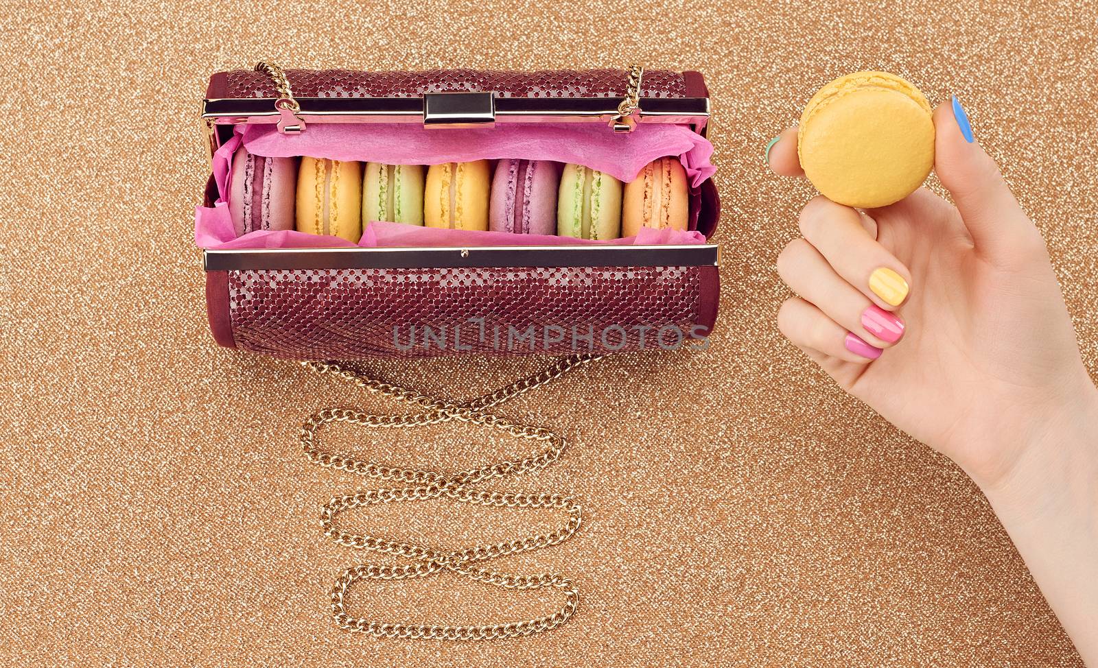Macarons french in handbag, woman hand. Luxury shiny glamor fashion clutch. Sweet colorful dessert. Unusual creative art, gold party background, bokeh, copyspase. Vintage