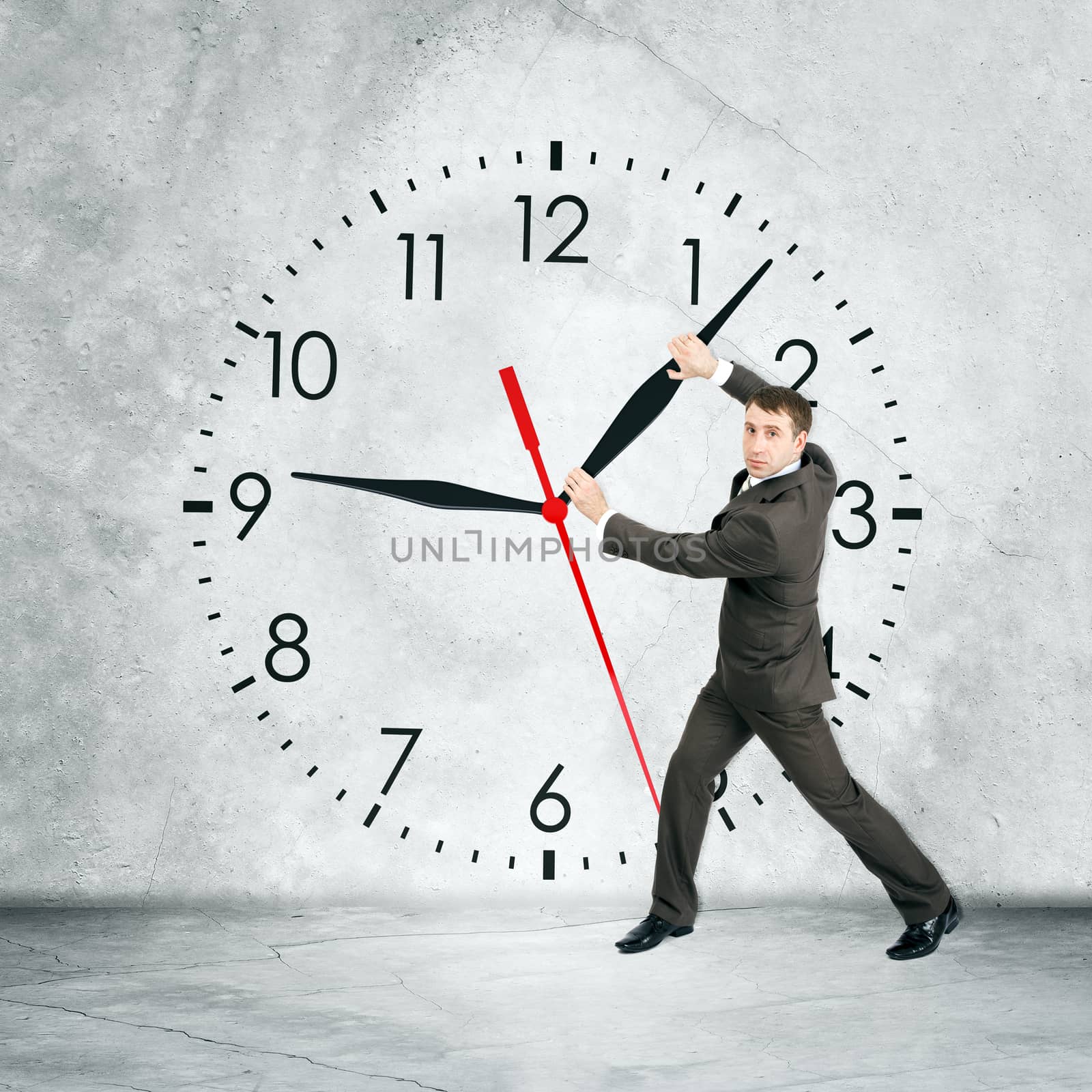 Businessman holding clock hand and looking at camera on grey wall backgound, rear view