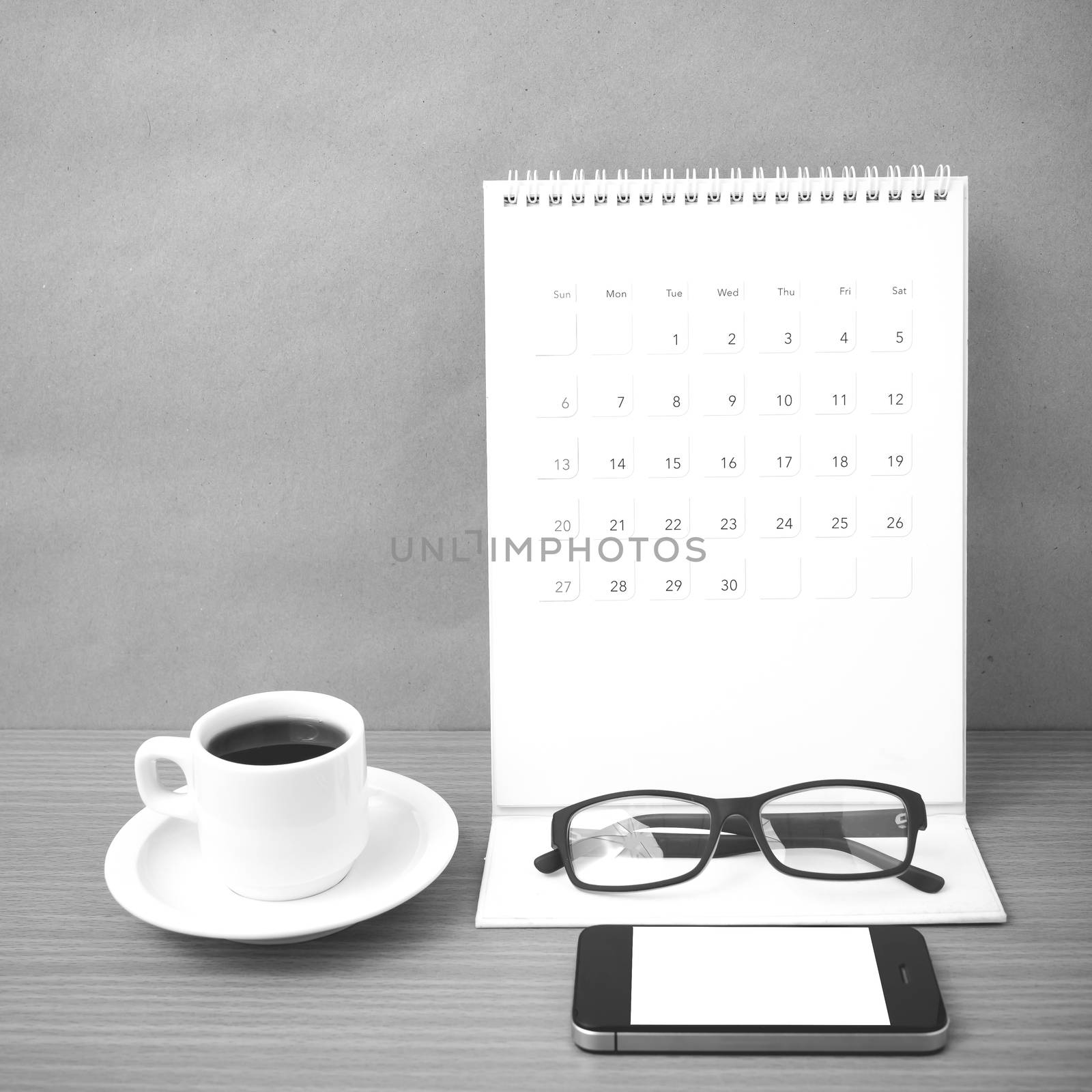 coffee,phone,eyeglasses and calendar on wood table background black and white color