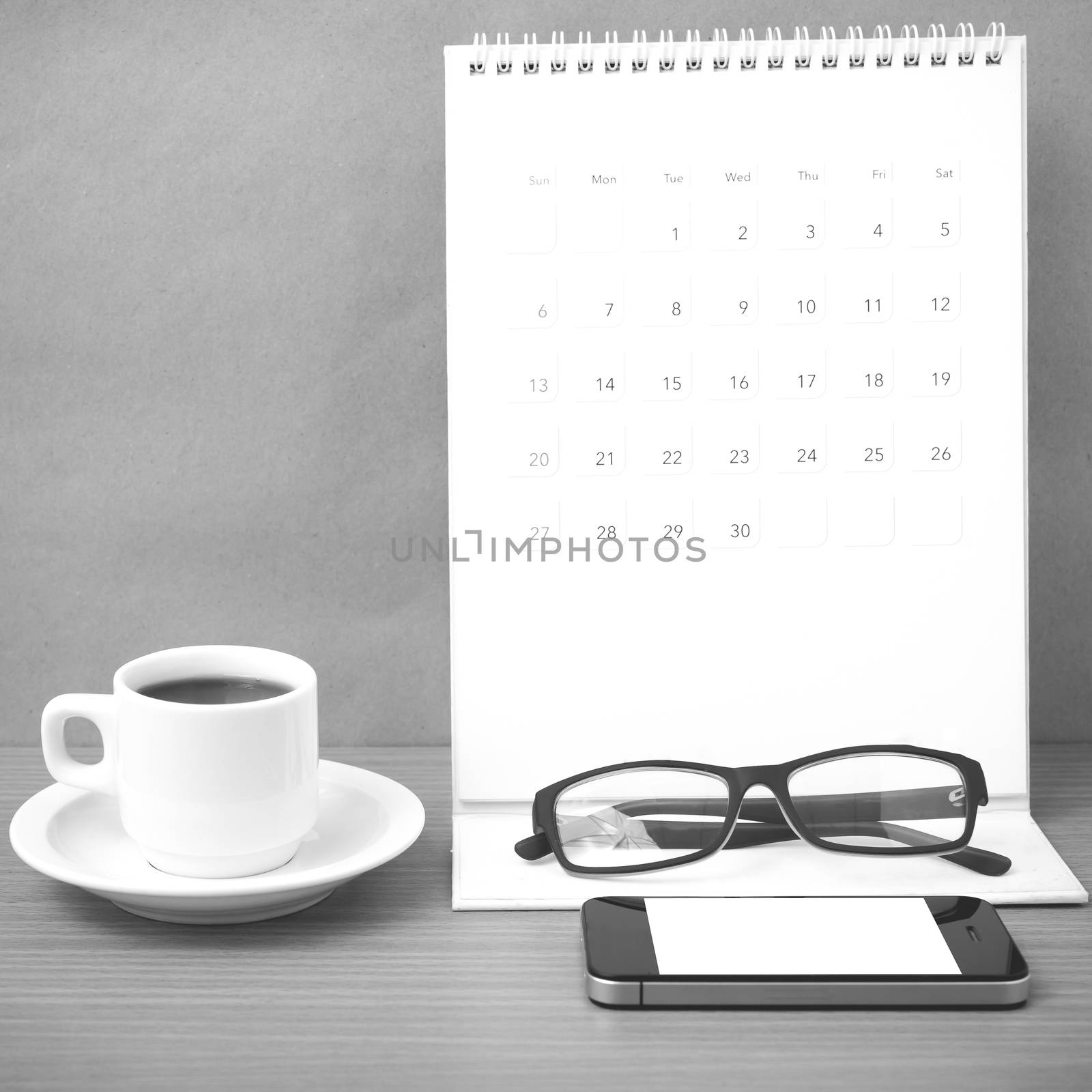 coffee,phone,eyeglasses and calendar on wood table background black and white color