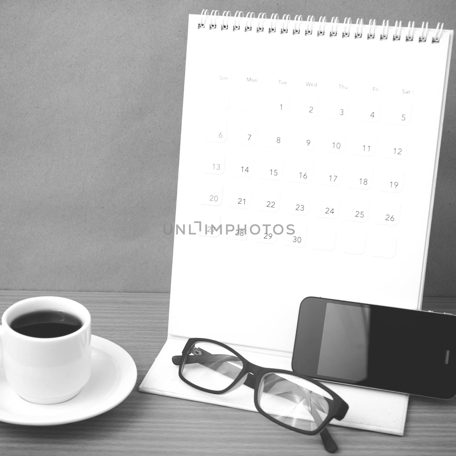 coffee,phone,eyeglasses and calendar on wood table background black and white color