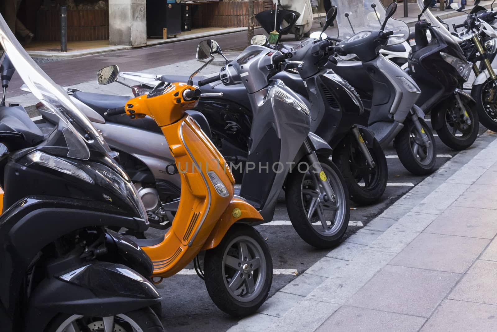 Many scooters on street, one of which is orange, and others are gray.