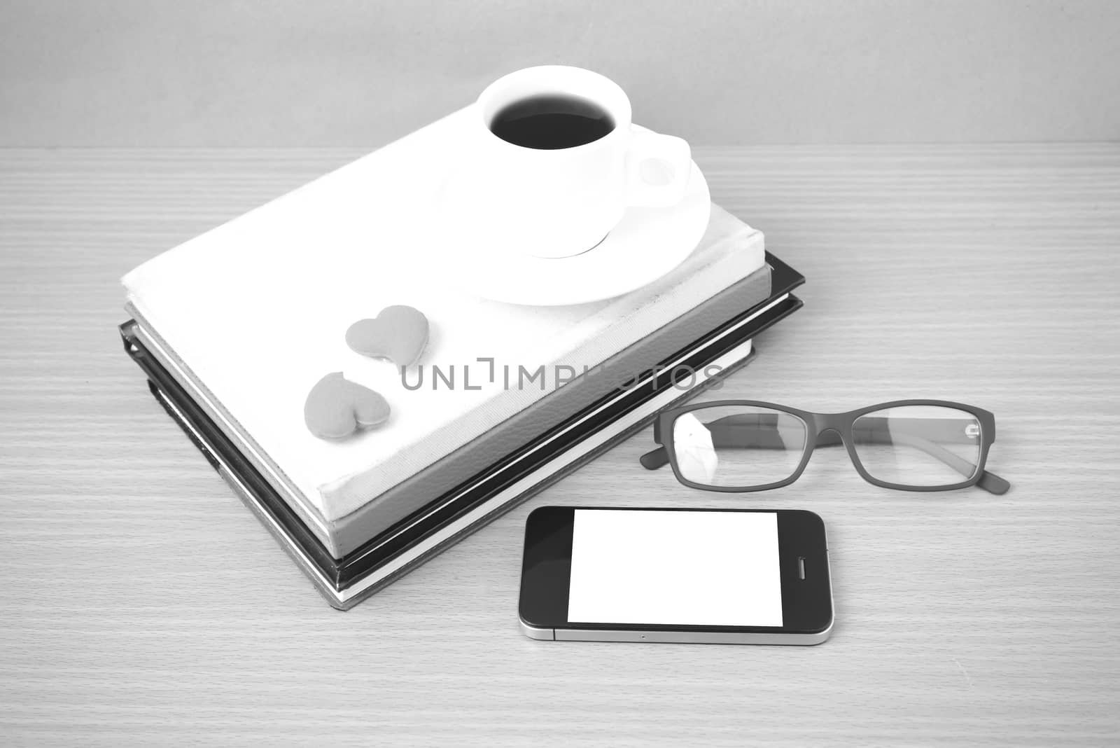 coffee,phone,eyeglasses,stack of book and heart on wood table background black  and white color