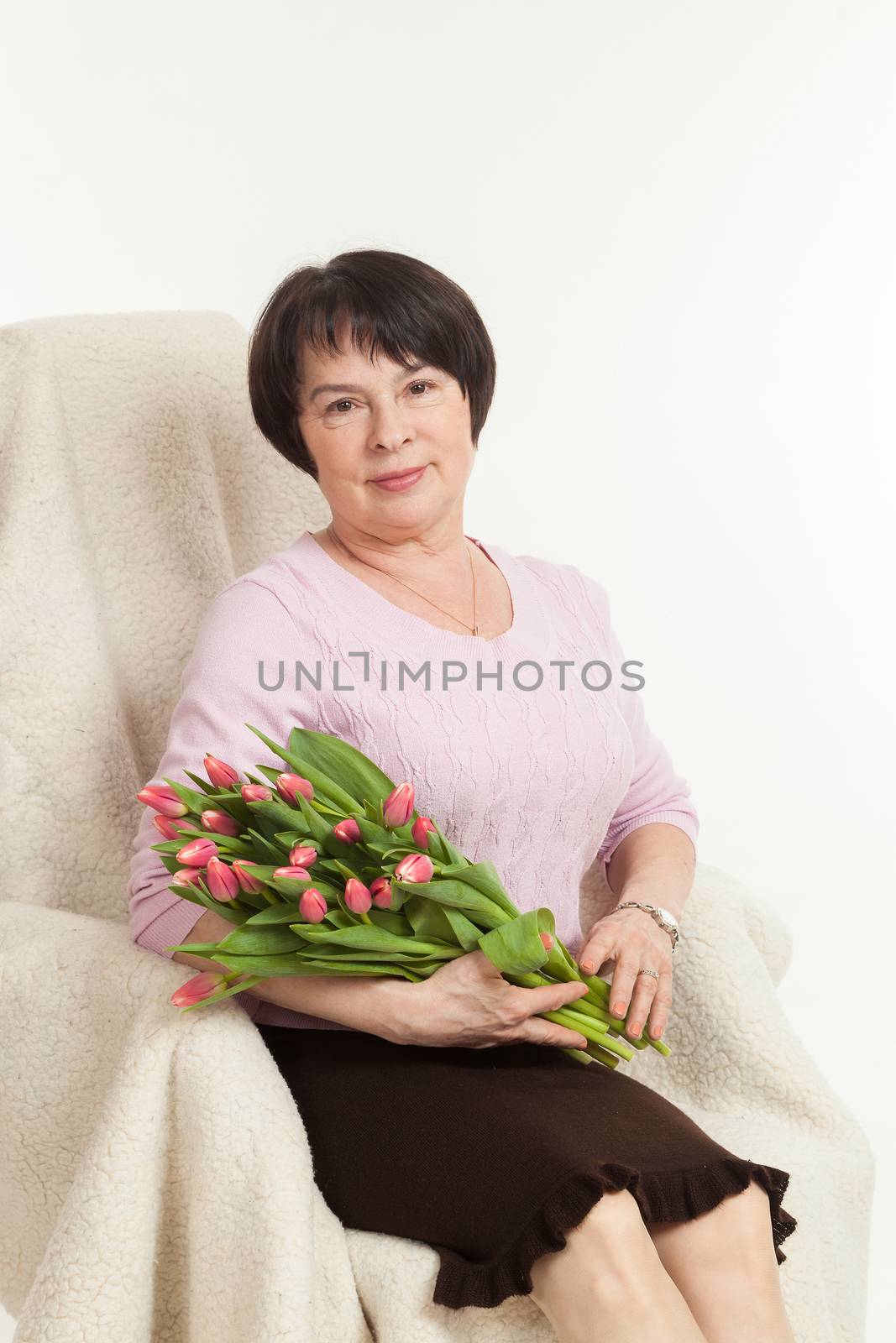 the beautiful mature woman sits on a chair with a bouquet of tulips