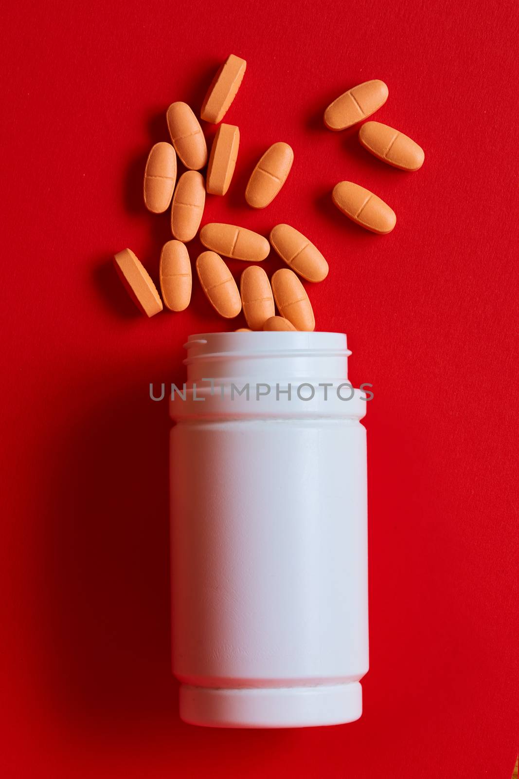 Pills spilling out of pill bottle on red. Top view with copy space. Medicine concept. Shallow dof