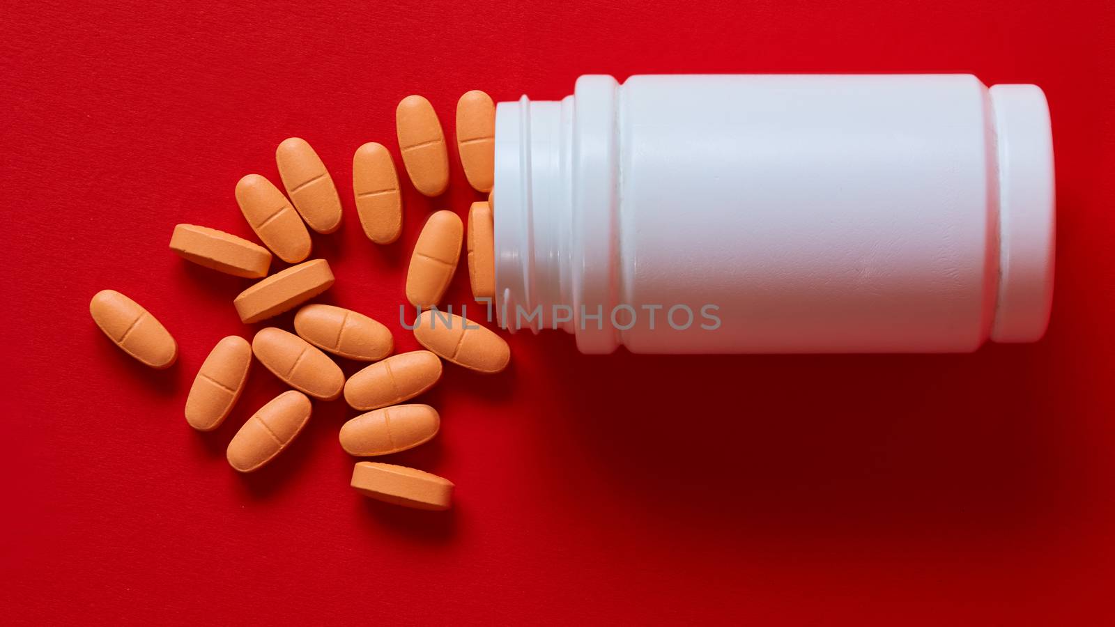 Pills spilling out of pill bottle on red. Top view with copy space.  by sarymsakov