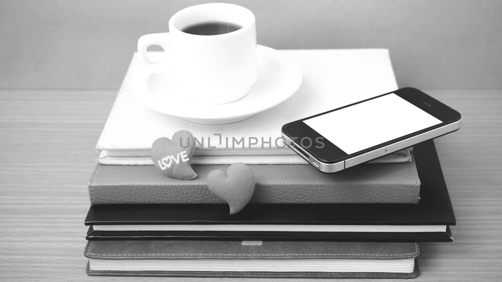 coffee,phone,stack of book and heart on wood table background black and white color