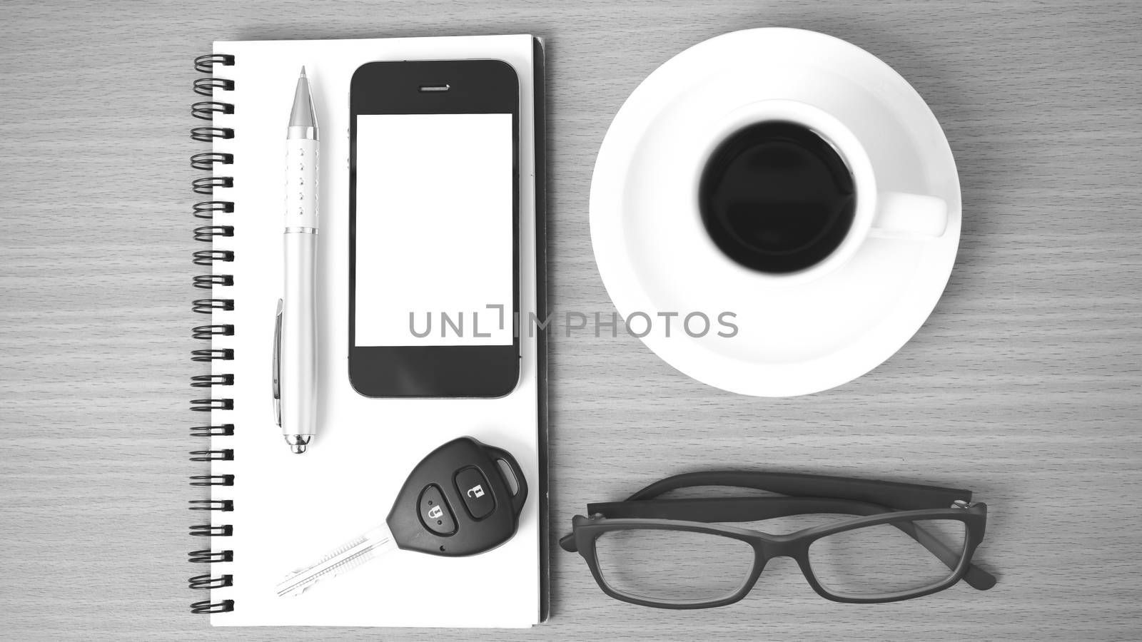 coffee,phone,notepad,eyeglasses and car key on wood table background black and white color