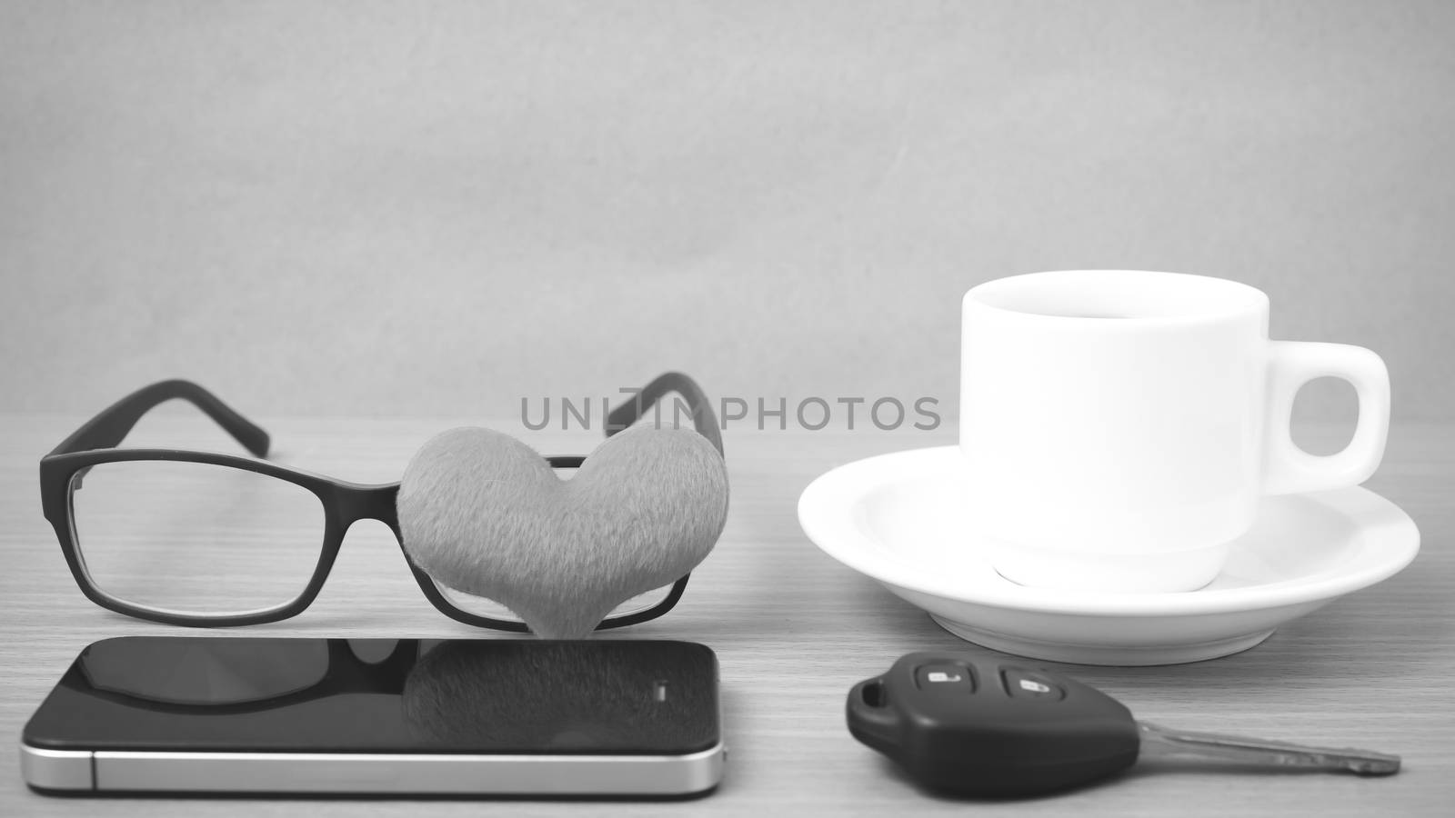 coffee,phone,eyeglasses and car key on wood table background black and white color