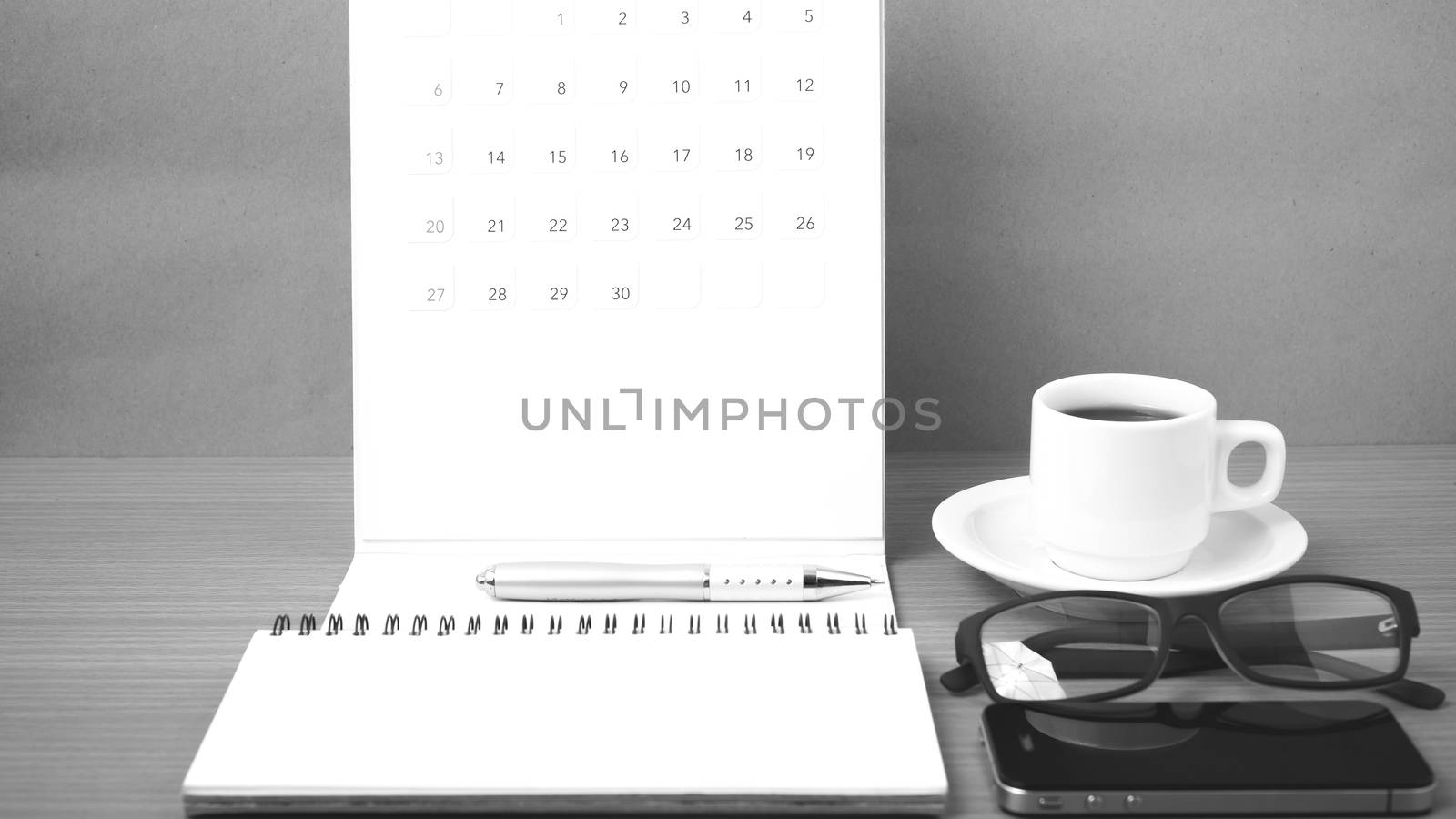 coffee,phone,eyeglasses,notepad and canlendar on wood table background black and white color