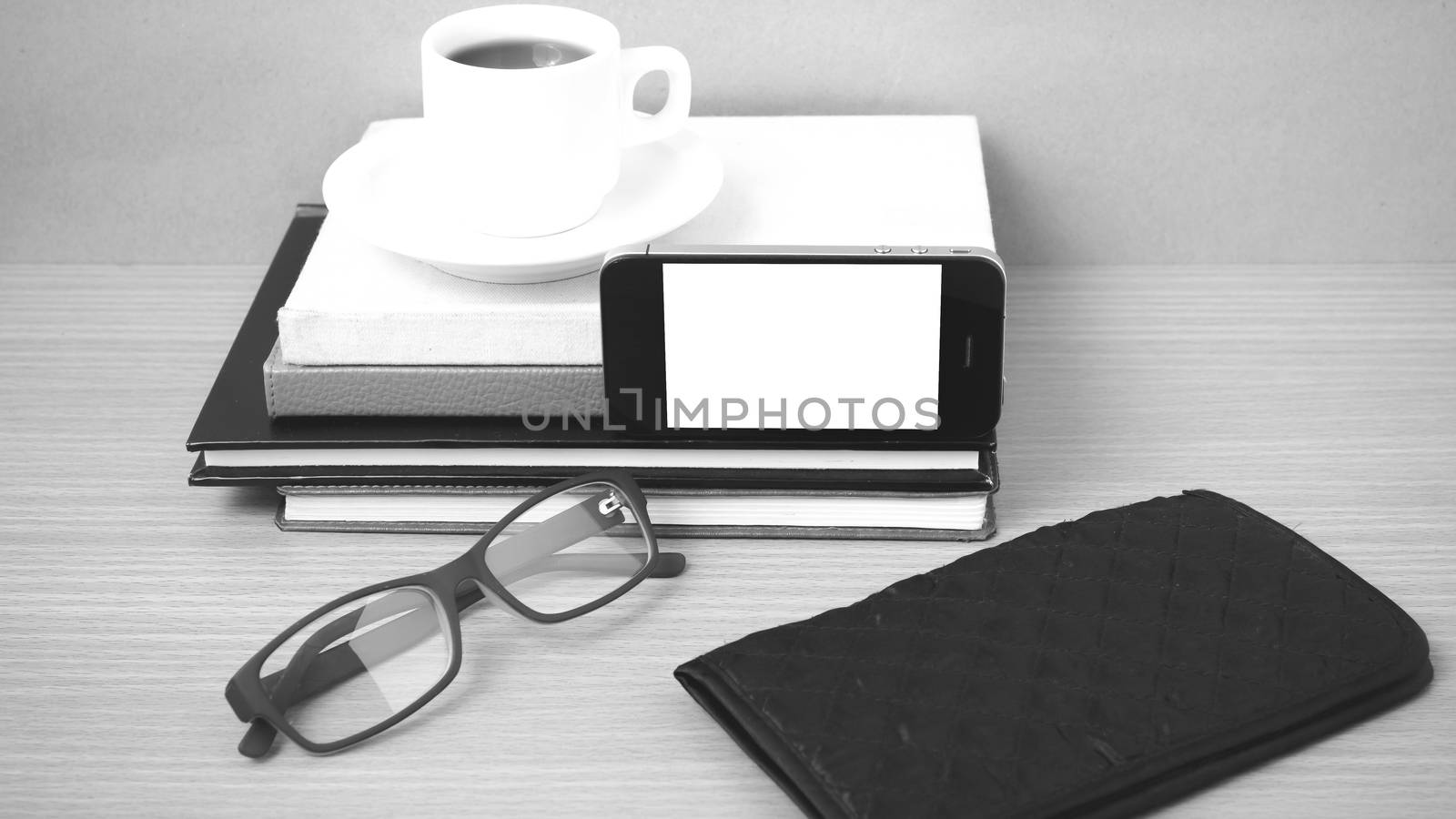 coffee,phone,eyeglasses,stack of book and wallet on wood table background black and white color