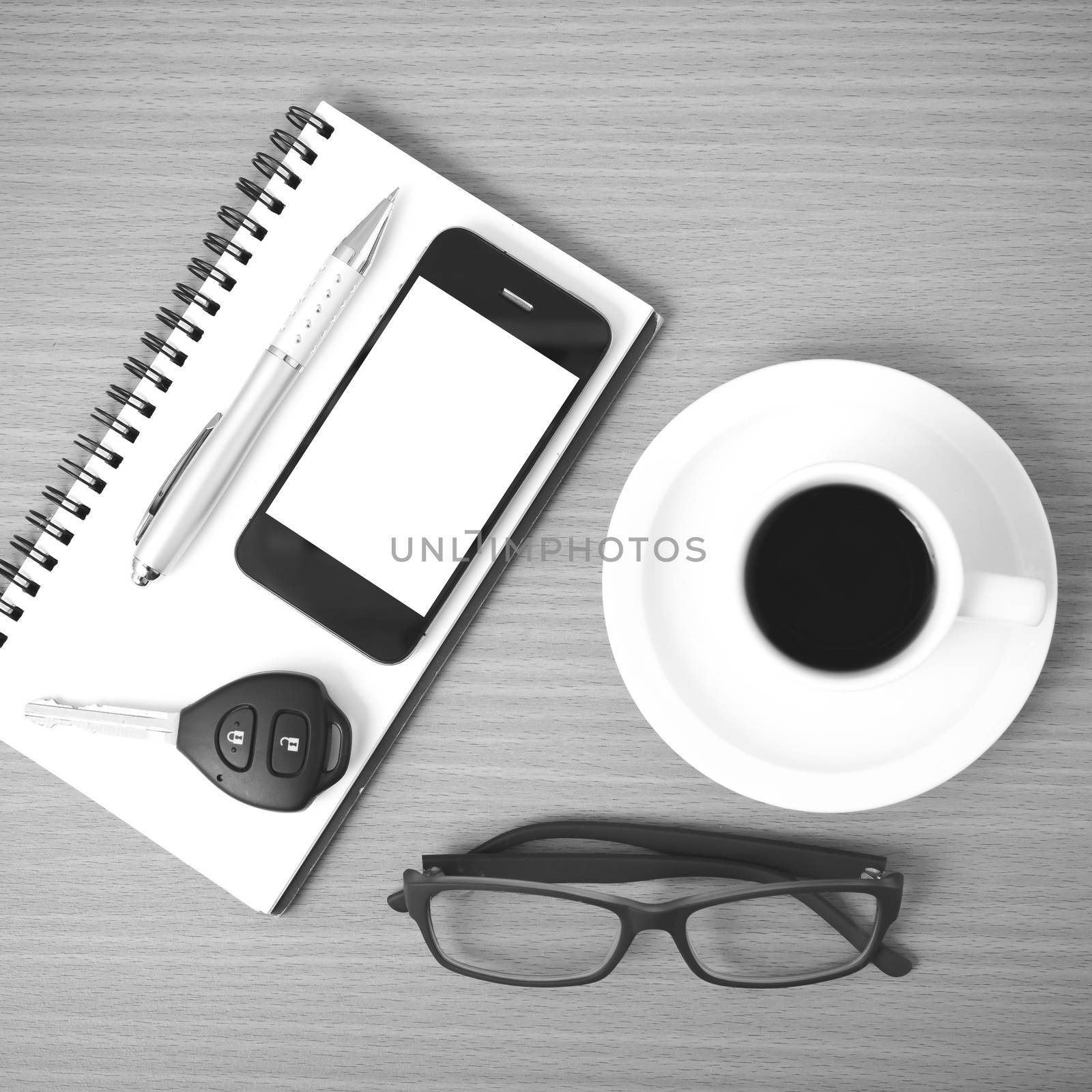 coffee,phone,notepad,eyeglasses and car key on wood table background black and white color
