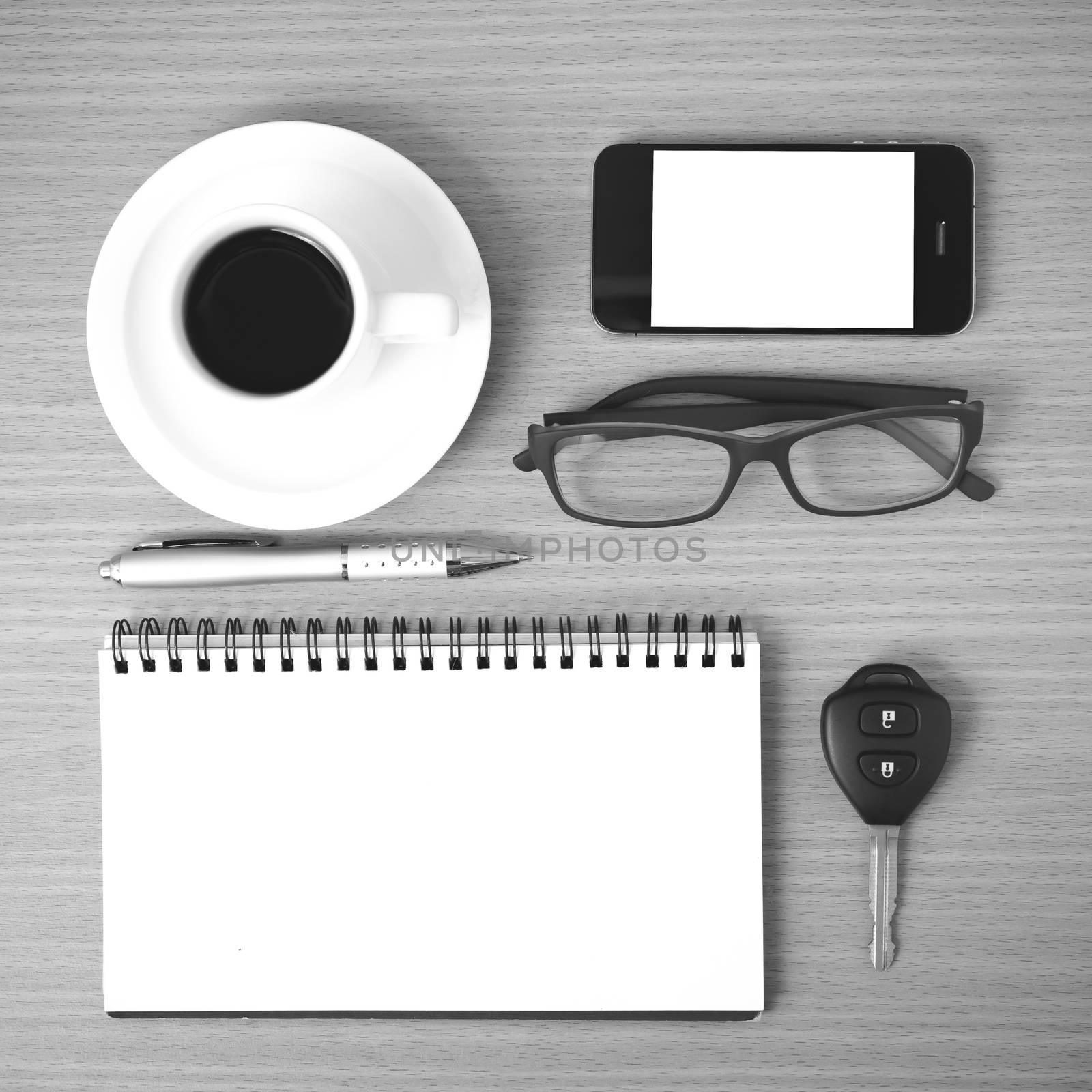 coffee,phone,notepad,eyeglasses and car key on wood table background black and white color