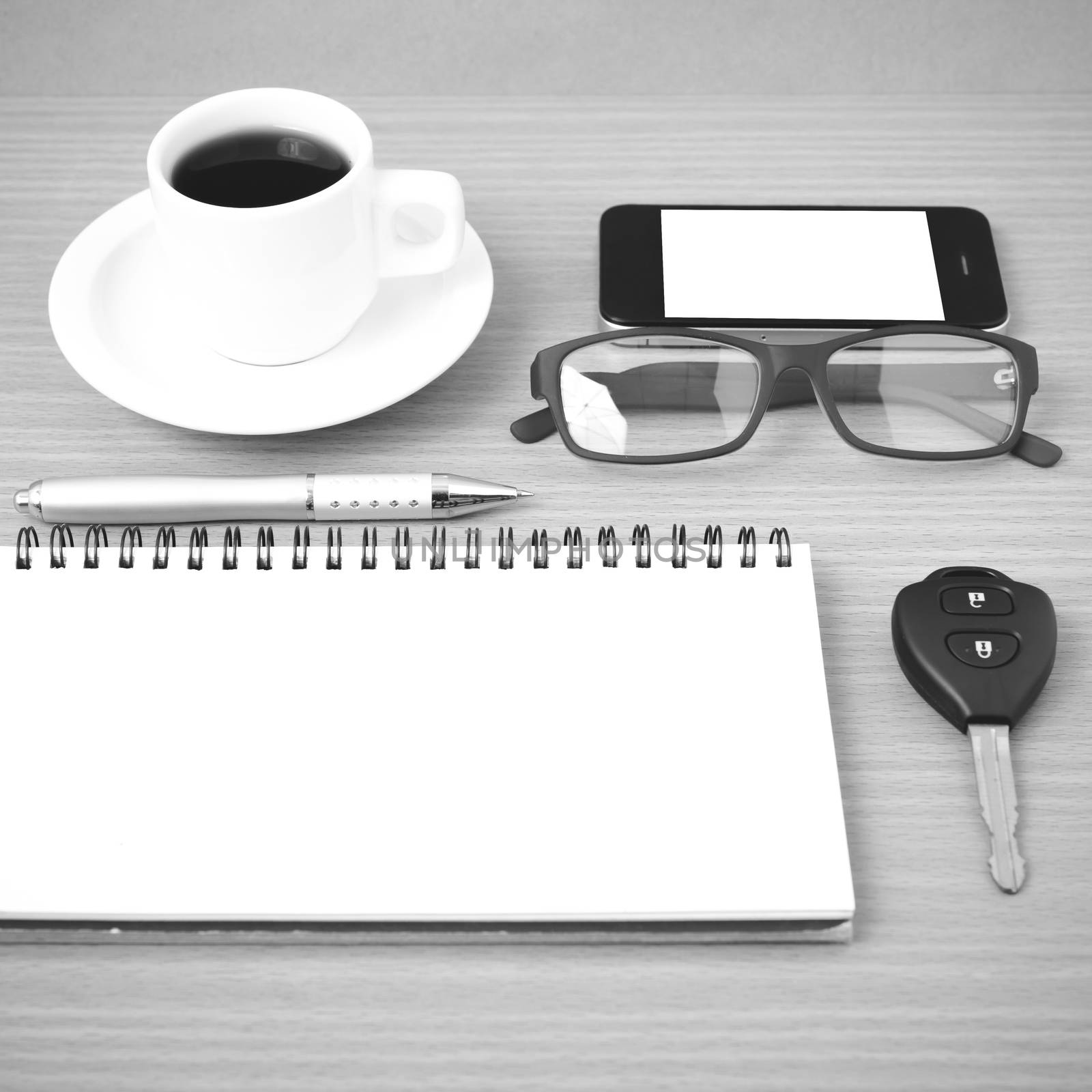 coffee,phone,notepad,eyeglasses and car key on wood table background black and white color