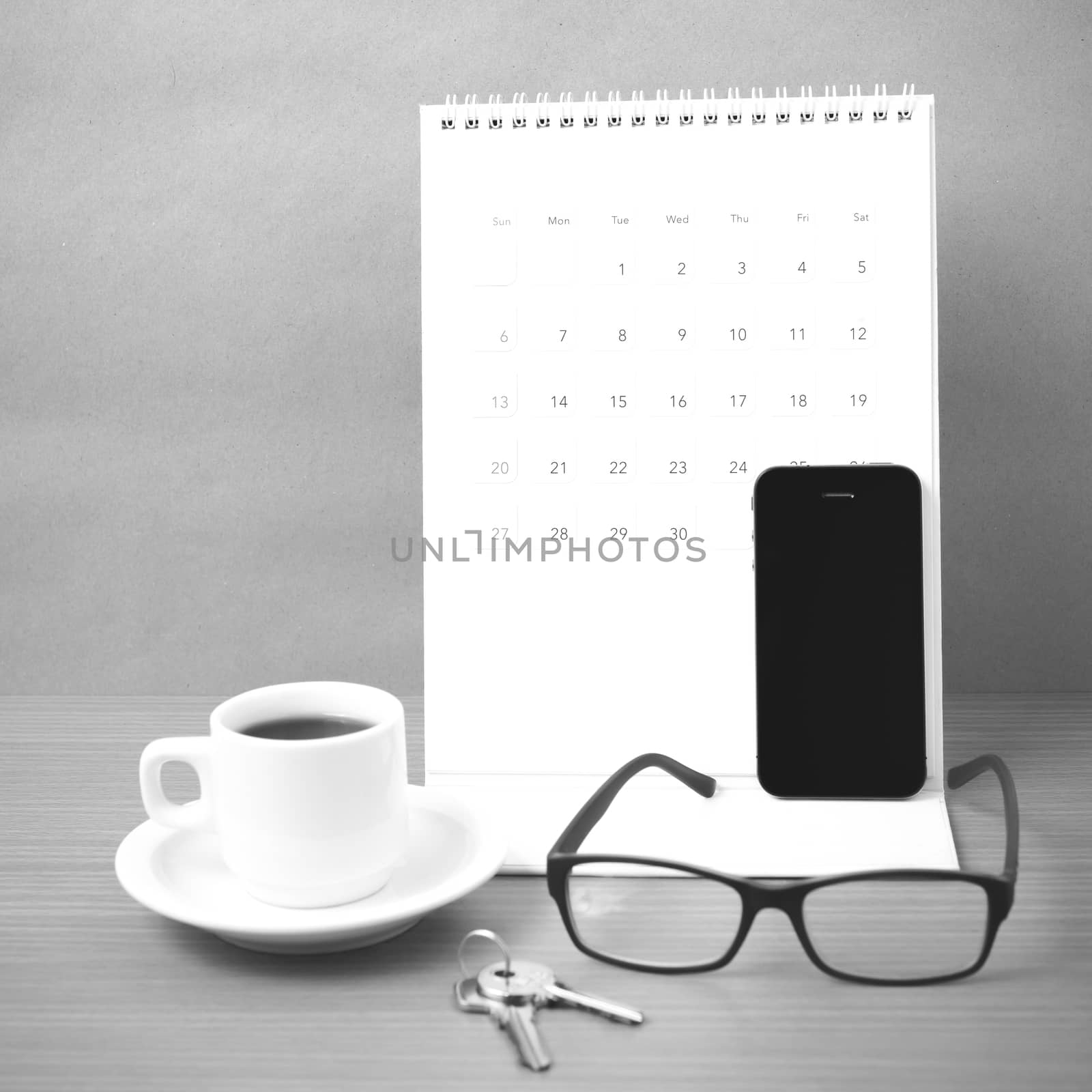 coffee,phone,eyeglasses,calendar and key on wood table background black and white color