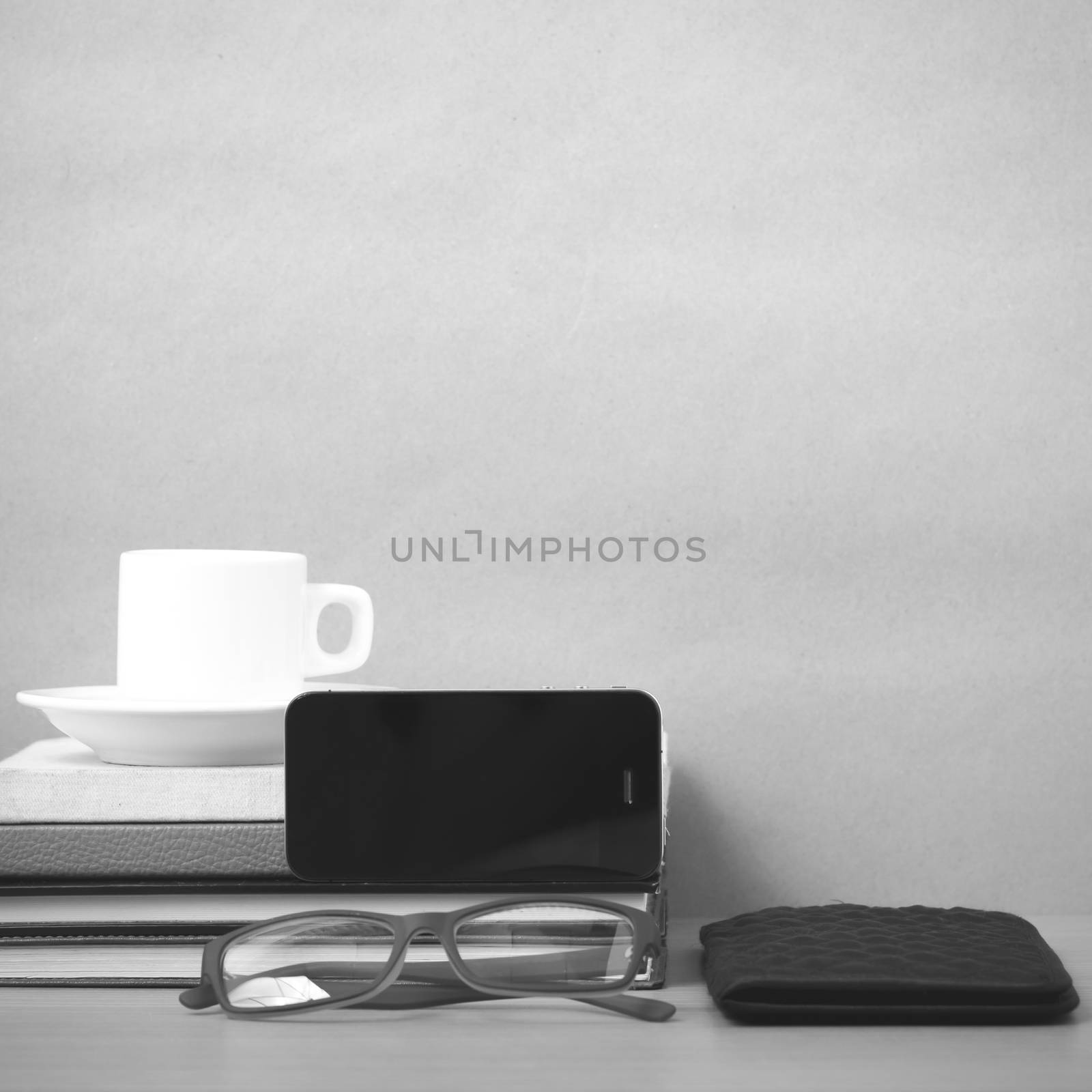 coffee,phone,eyeglasses,stack of book and wallet on wood table background black and white color