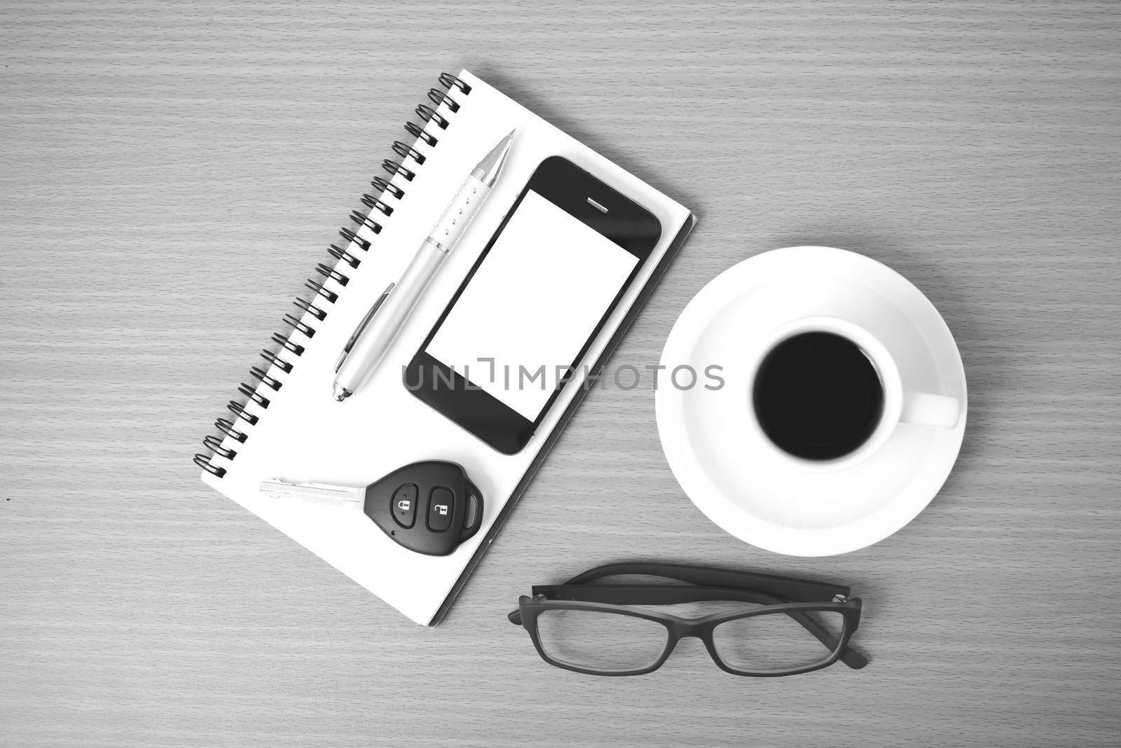 coffee,phone,notepad,eyeglasses and car key on wood table background black and white color