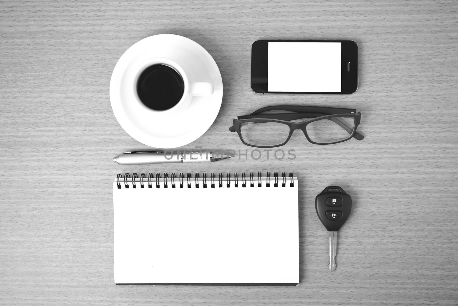 coffee,phone,notepad,eyeglasses and car key on wood table background black and white color