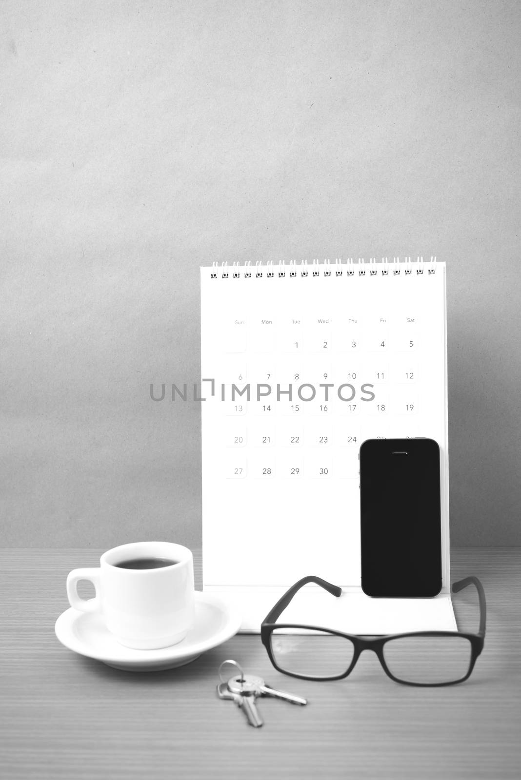 coffee,phone,eyeglasses,calendar and key on wood table background black and white color