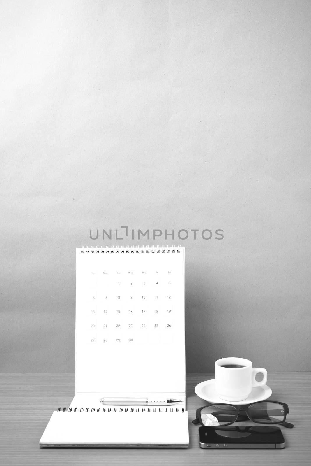 coffee,phone,eyeglasses,notepad and canlendar on wood table background black and white color