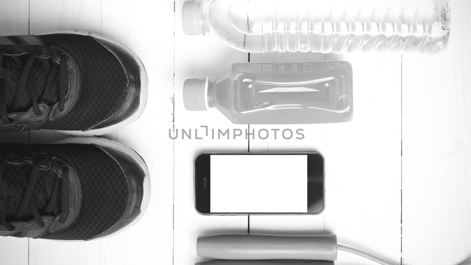 fitness equipment : running shoes,jumping rope,water,juice and phone on white wood background black and white color