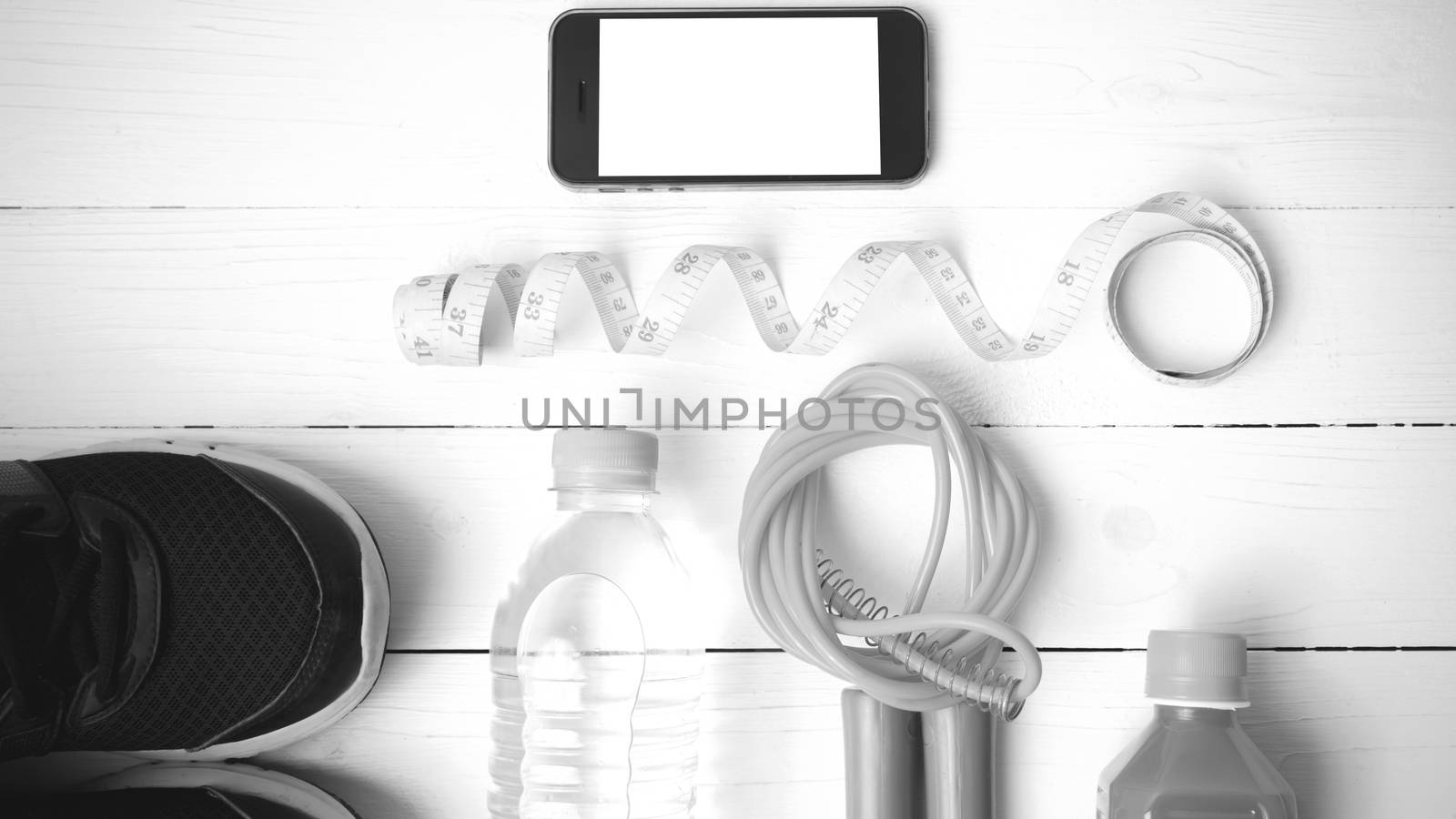 fitness equipment:running shoes,phone,measuring tape,water,juice and jumpong rope on white wood background black and white color