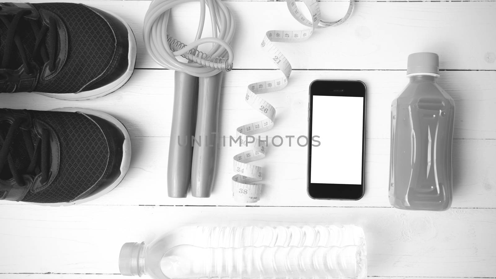 fitness equipment:running shoes,phone,measuring tape,water,juice and jumpong rope on white wood background black and white color