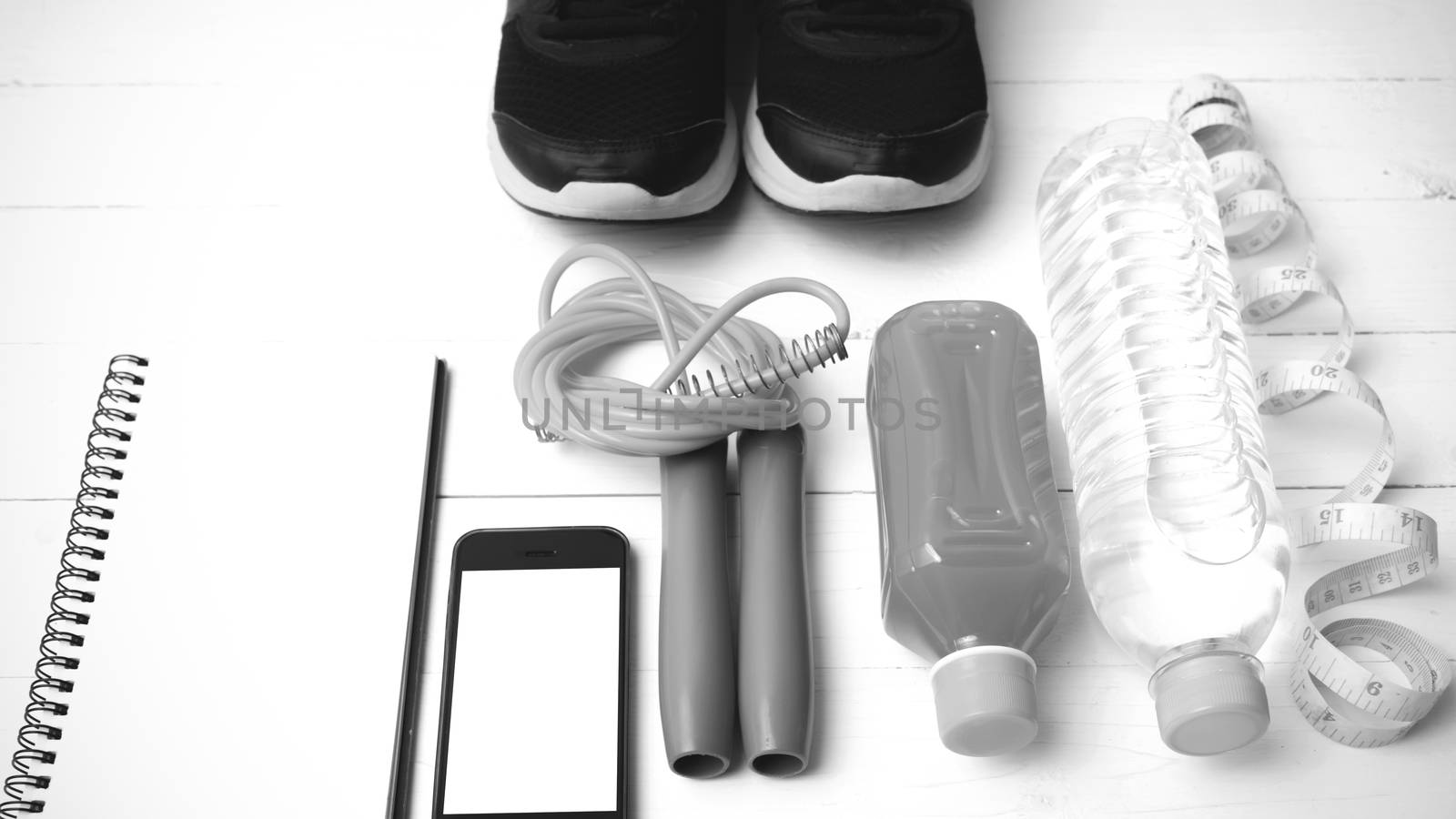 fitness equipment:running shoes,jumping rope,notepad,phone,water,juice and measuring tape on white wood background black and white color