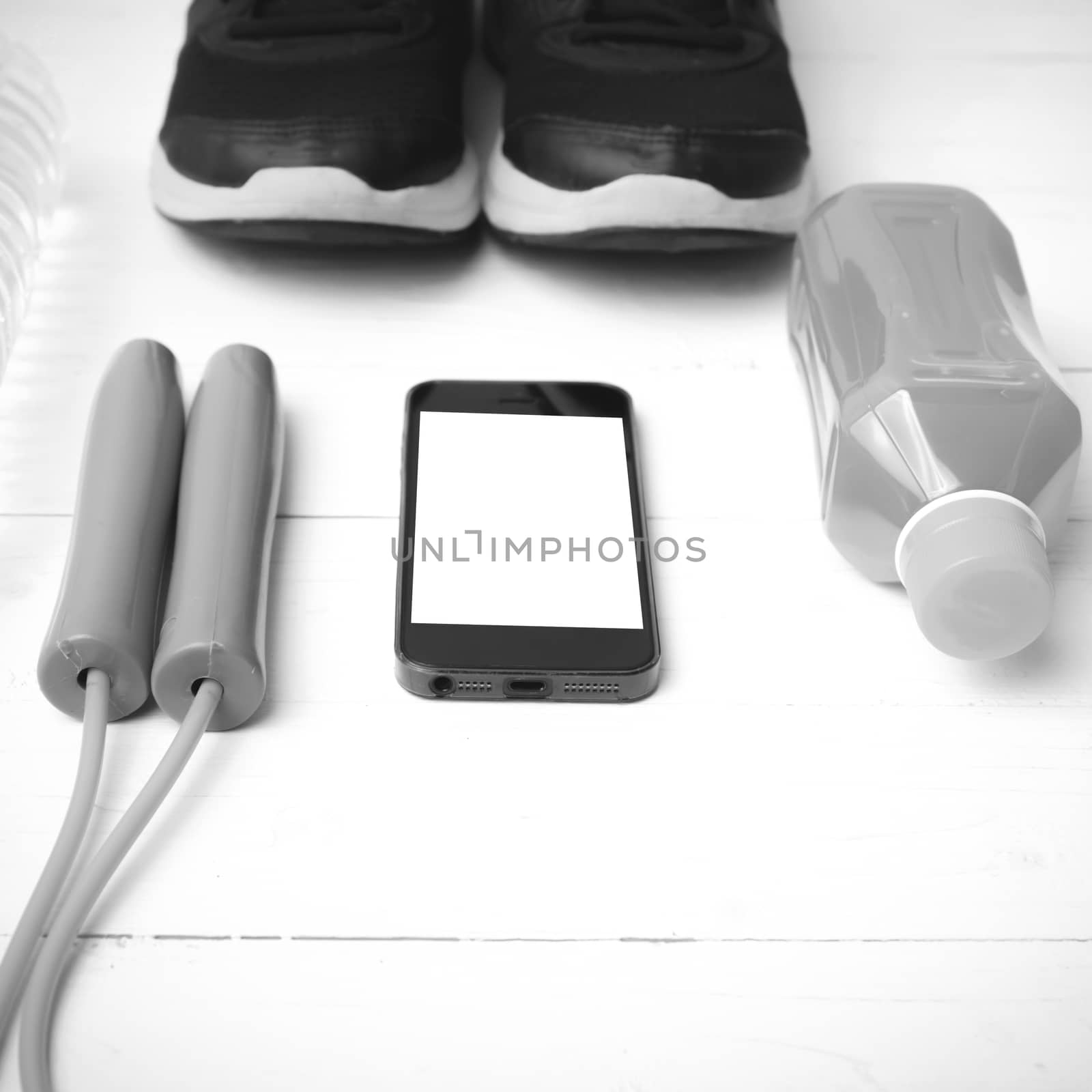 fitness equipment : running shoes,jumping rope,water,juice and phone on white wood background black and white color