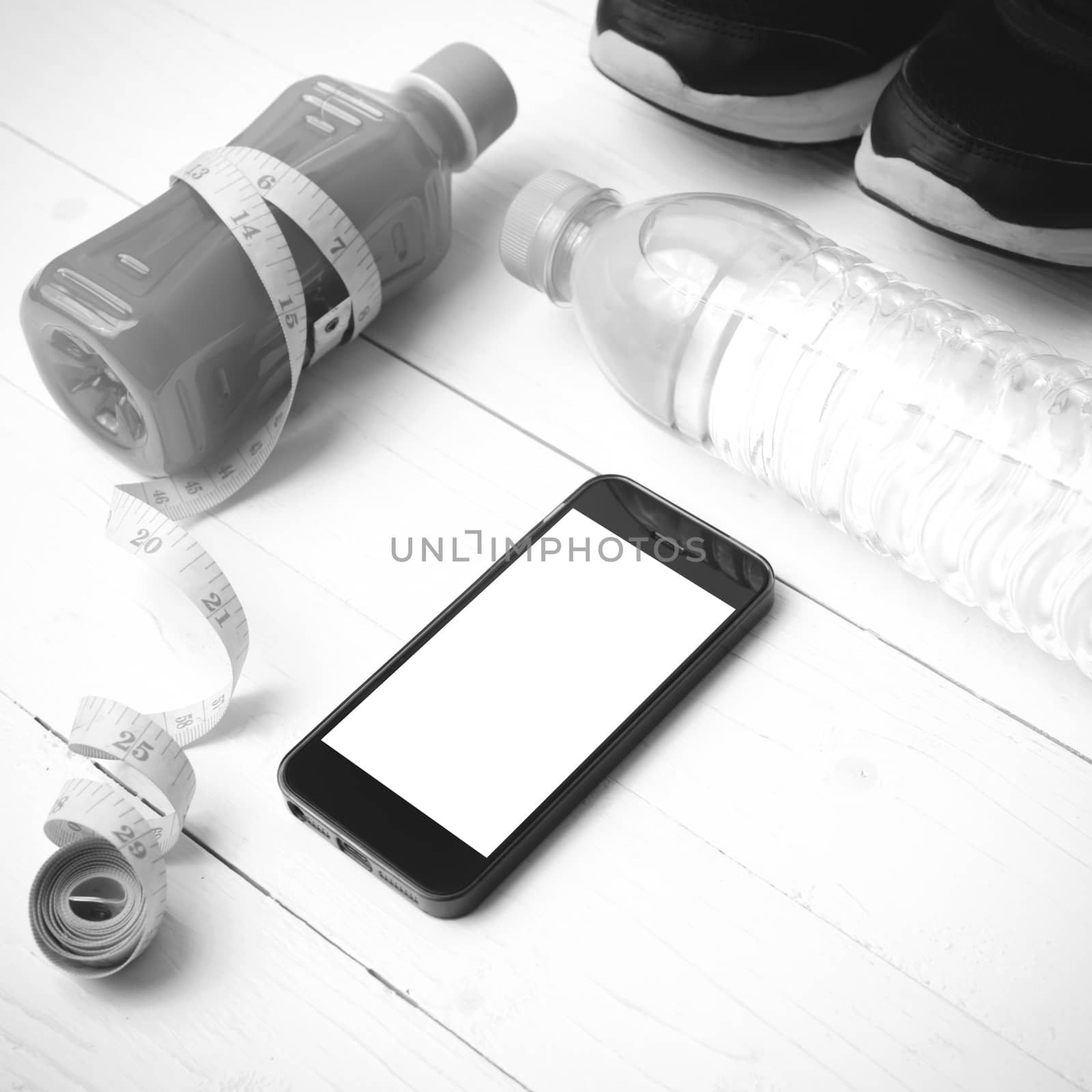 fitness equipment:running shoes,measuring tape,water,juice and phone on white wood background black and white color