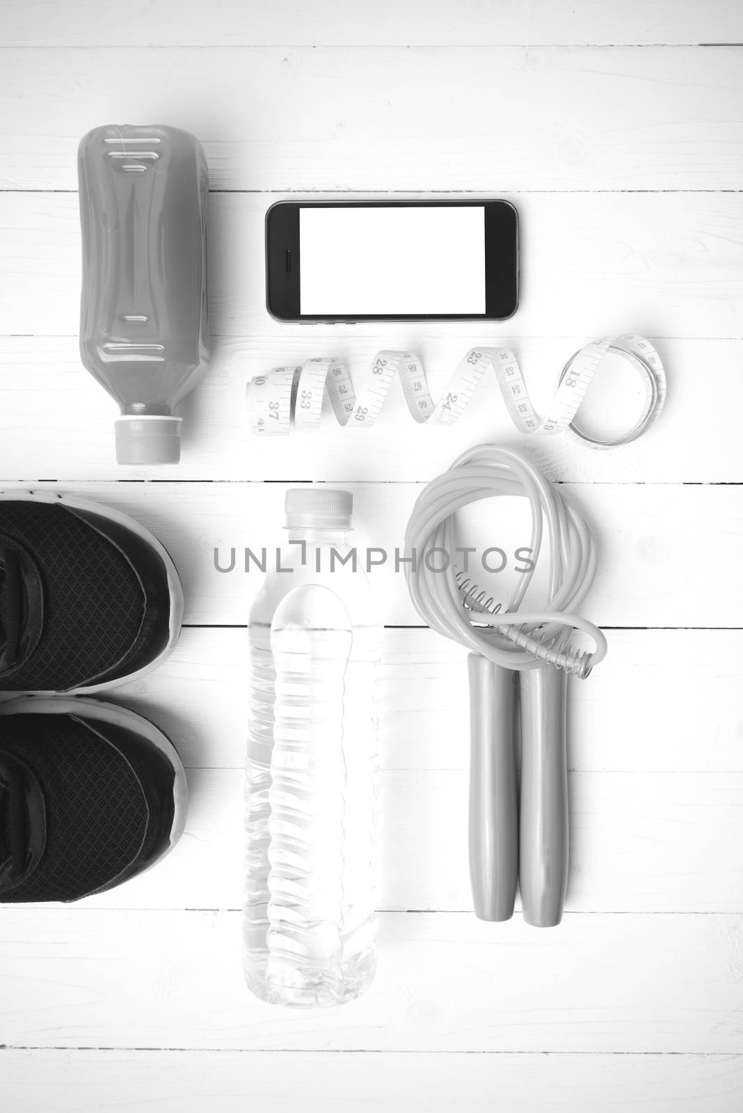 fitness equipment:running shoes,phone,measuring tape,water,juice and jumpong rope on white wood background black and white color