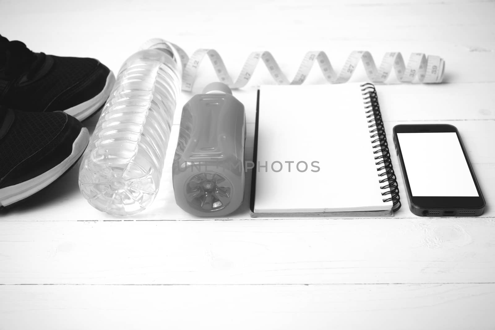 fitness equipment:running shoes,water,measuring tape,notepad,phone and juice on white wood background black and white color