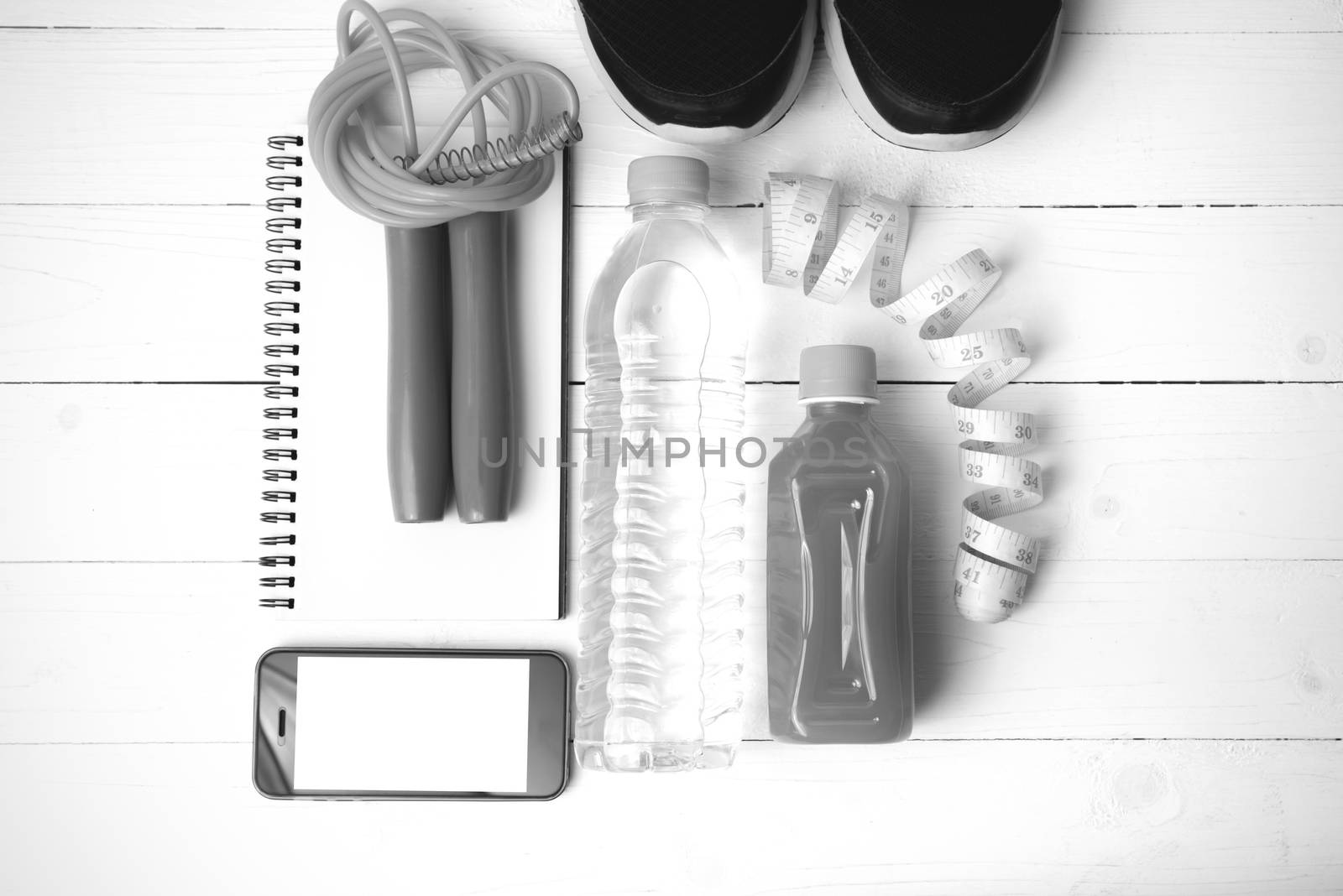 fitness equipment:running shoes,jumping rope,notepad,phone,water,juice and measuring tape on white wood background black and white color