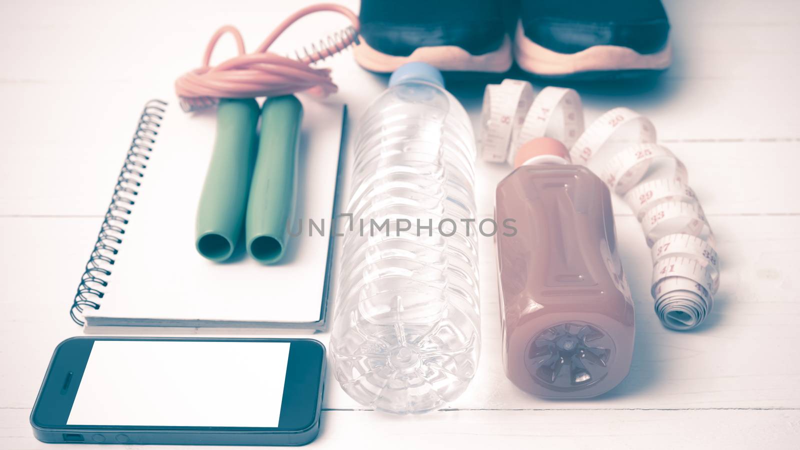 fitness equipment:running shoes,jumping rope,notepad,phone,water,juice and measuring tape on white wood background vintage style