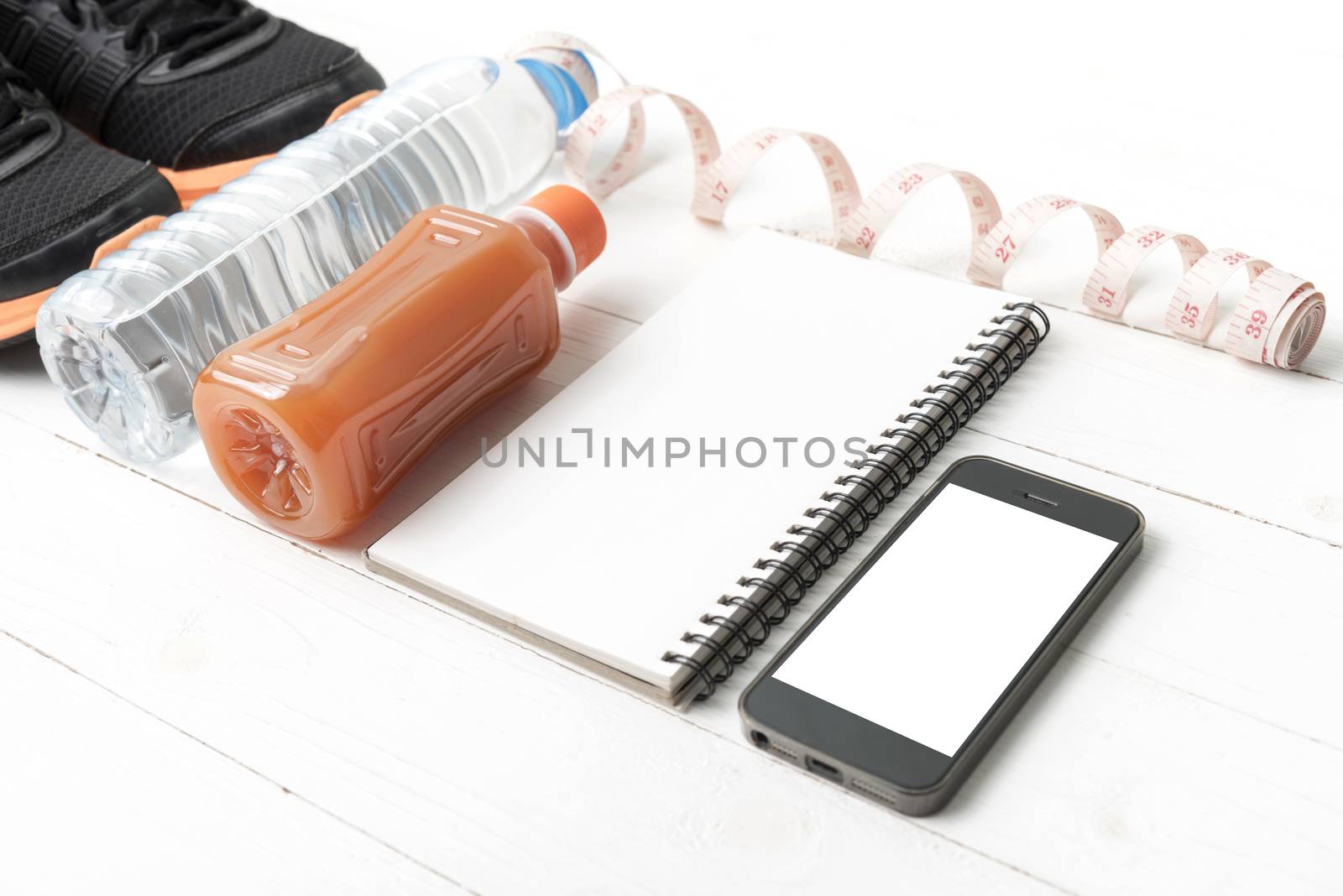 fitness equipment:running shoes,water,measuring tape,notepad,phone and juice on white wood background