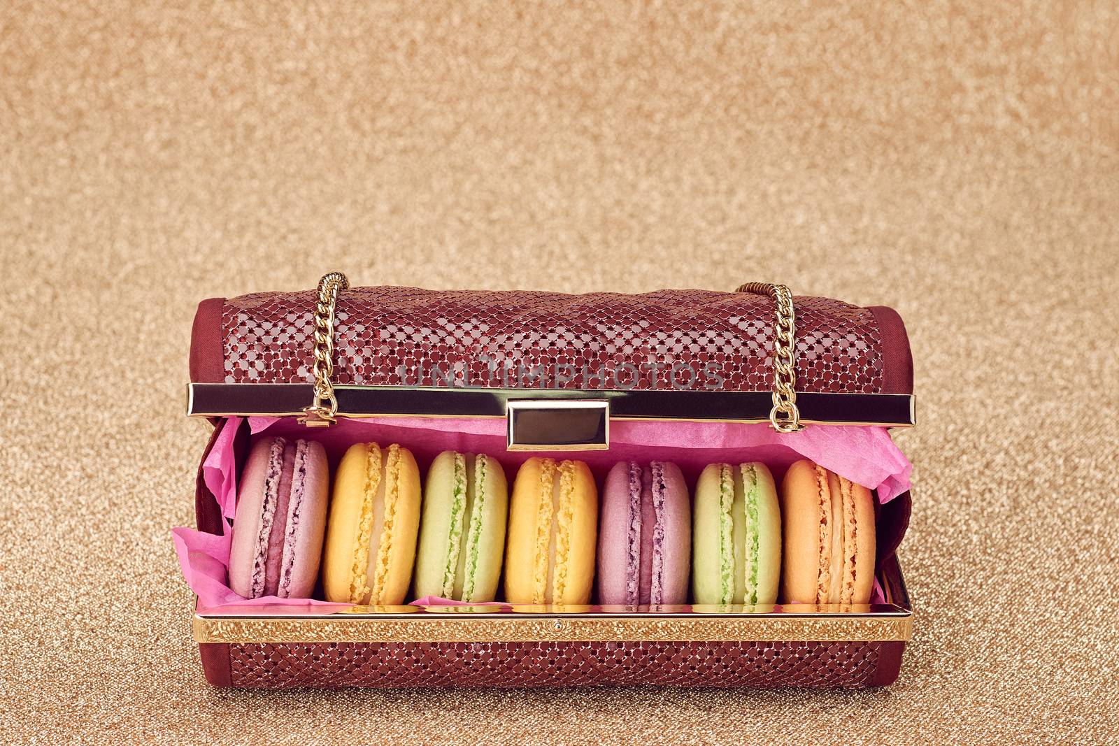 Macarons french in handbag. Luxury shiny glamor fashion clutch. Sweet colorful dessert. Unusual creative art, gold party background, bokeh, closeup. Vintage