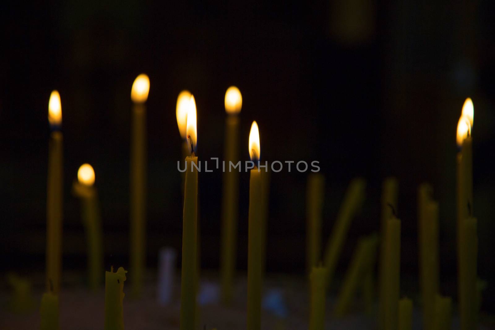 Lighted wax candles in a church burning in the twilight