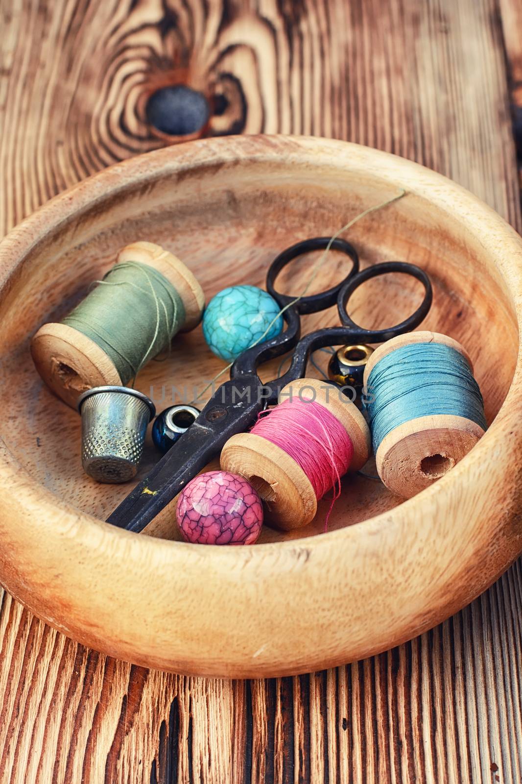 Scissors,buttons and thread in wooden bowl on background of pine.