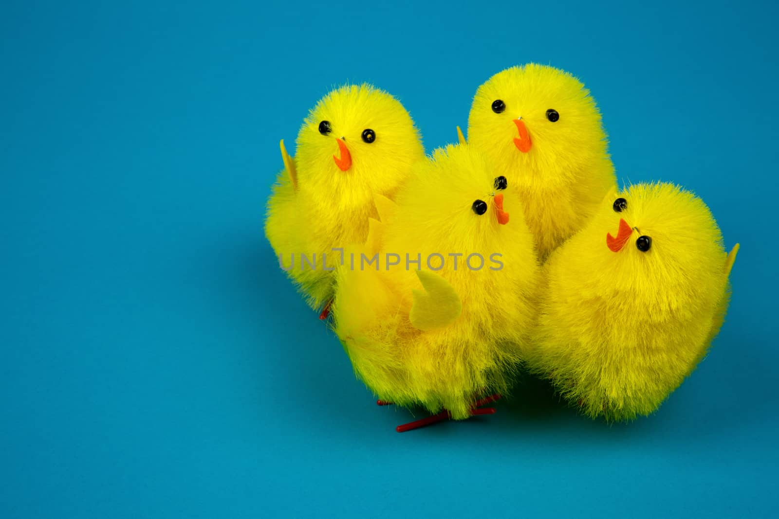 Four yellow Easter chickens figurines close to each other on a blue background, easter decoration or poostcard. Close, horizontal view.