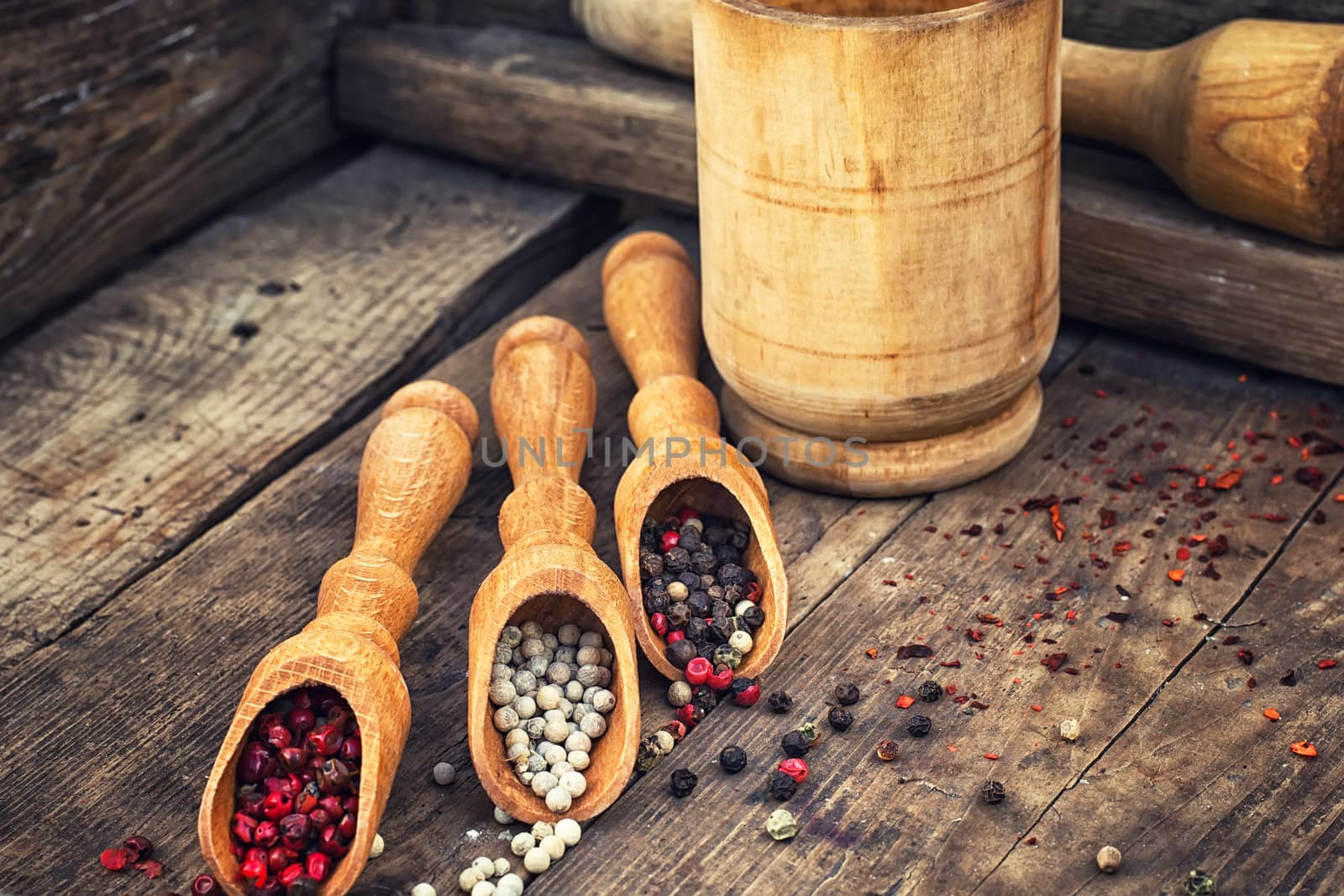 Three kinds of pepper in wooden spoons on vintage background