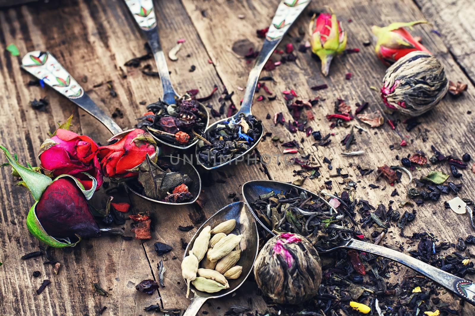 Varieties of tea brewed in an iron spoon on wooden background with buds of tea roses