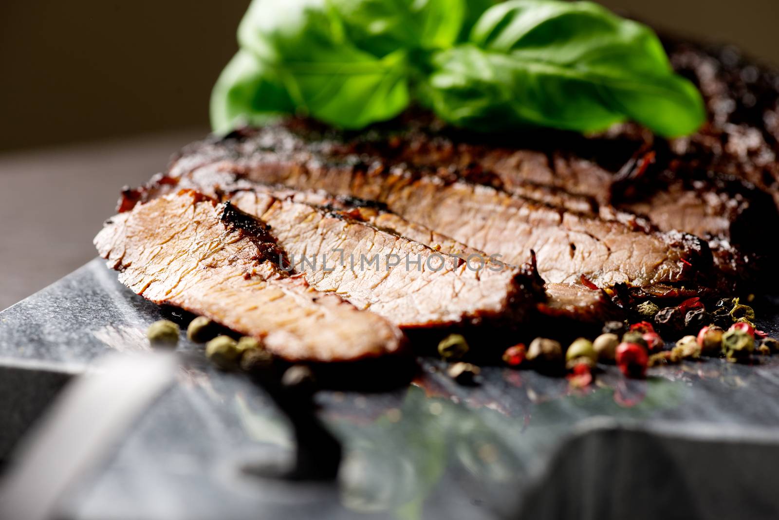 Close up sliced medium grilled beef steak with pepper and oregano leafs on marble meat cutting board on dark stone background