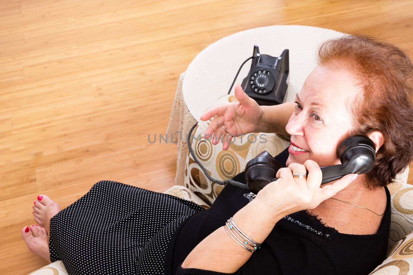 Grandma sitting in a comfortable armchair at home chatting on an old rotary telephone and smiling happily as she socialises with a friend, high angle view