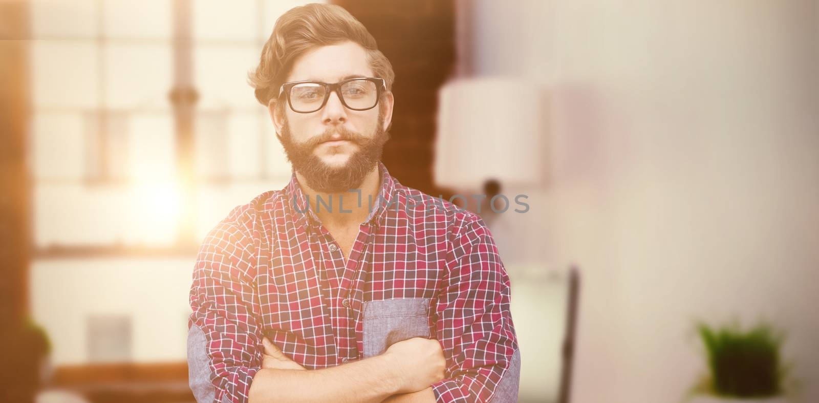 Confident hipster wearing eye glasses with arms crossed against laptop on desk with glasses and notepad