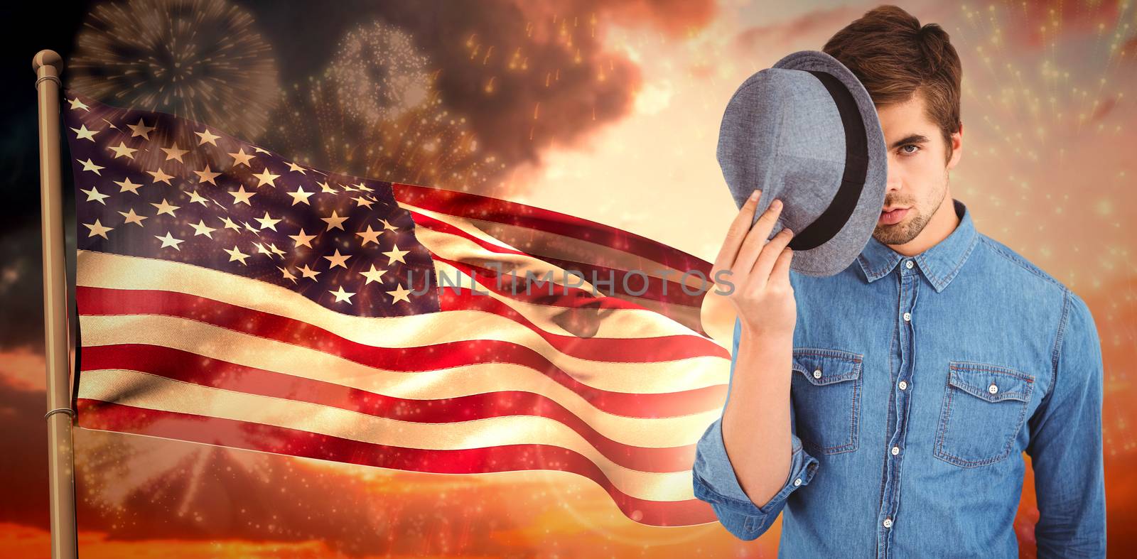 Portrait of hipster holding hat in front of face against composite image of lens flare