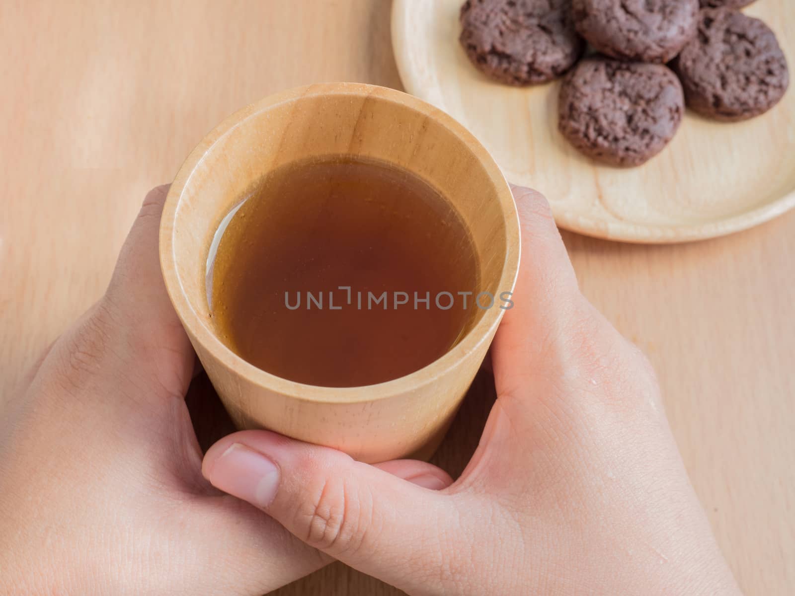 Closeup of female hands holding wood cup of Organic Jasmine Tea with cookies
