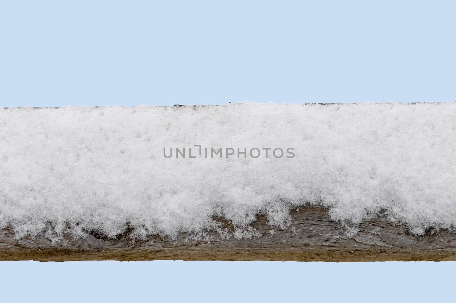 Snow covered old wood fence railing with a light blue sky background