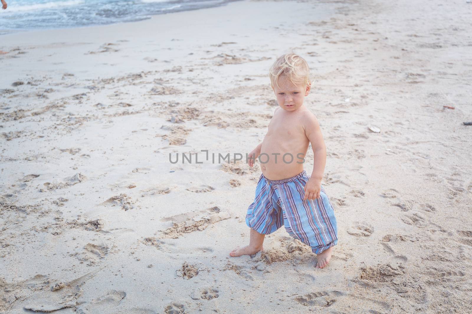 Toddler in a blue pants walking on a white sand in Thailand