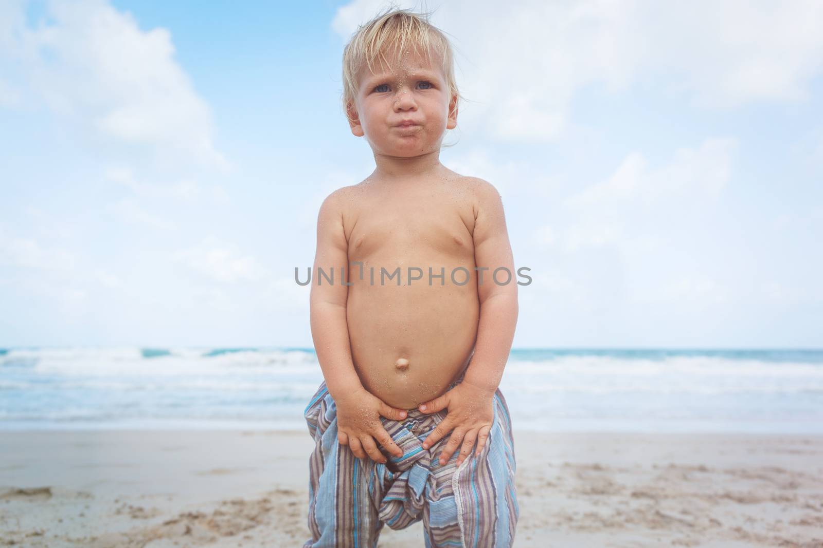 Little boy walking barefoot on white sand beach