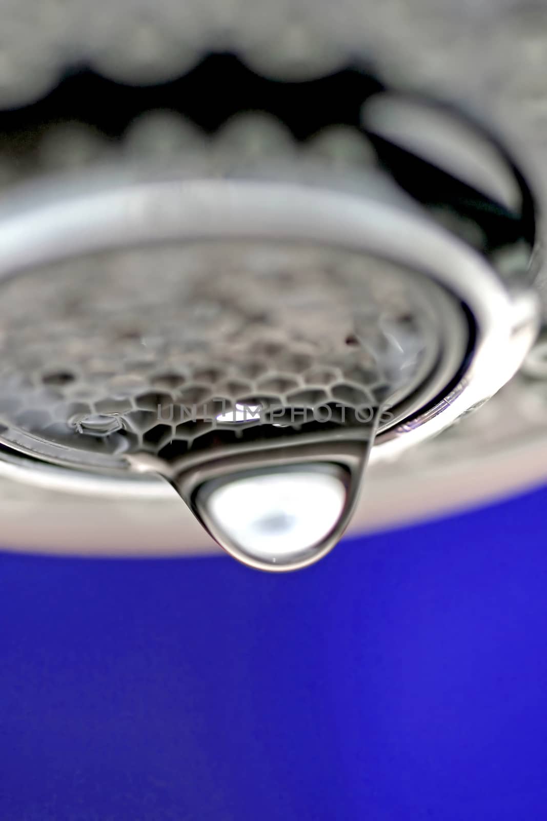 A macro of a white tap / faucet dripping with blue background.